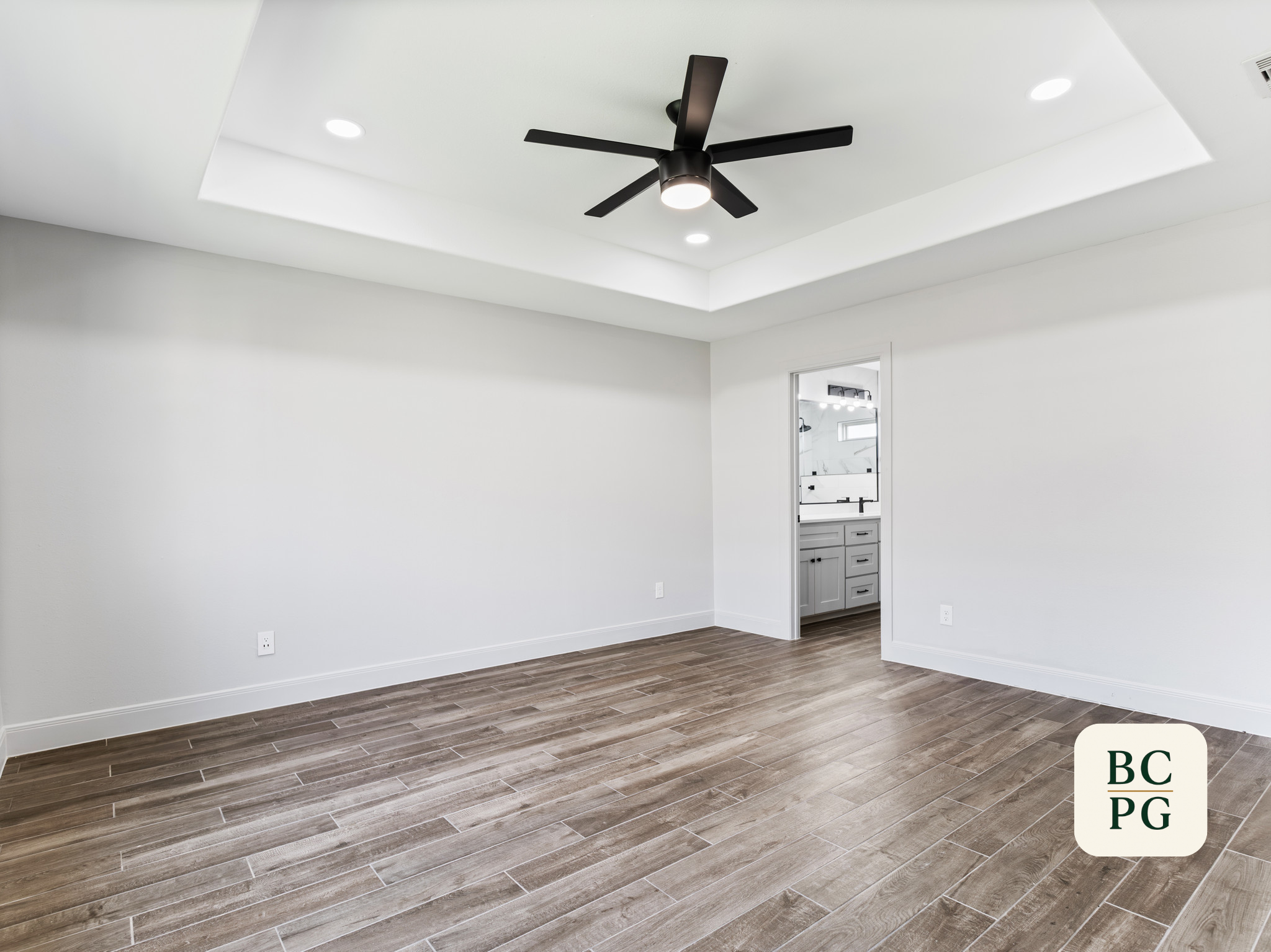 A modern interior room with white walls and ceiling, brown wooden flooring, ceiling fans, and recessed lighting.