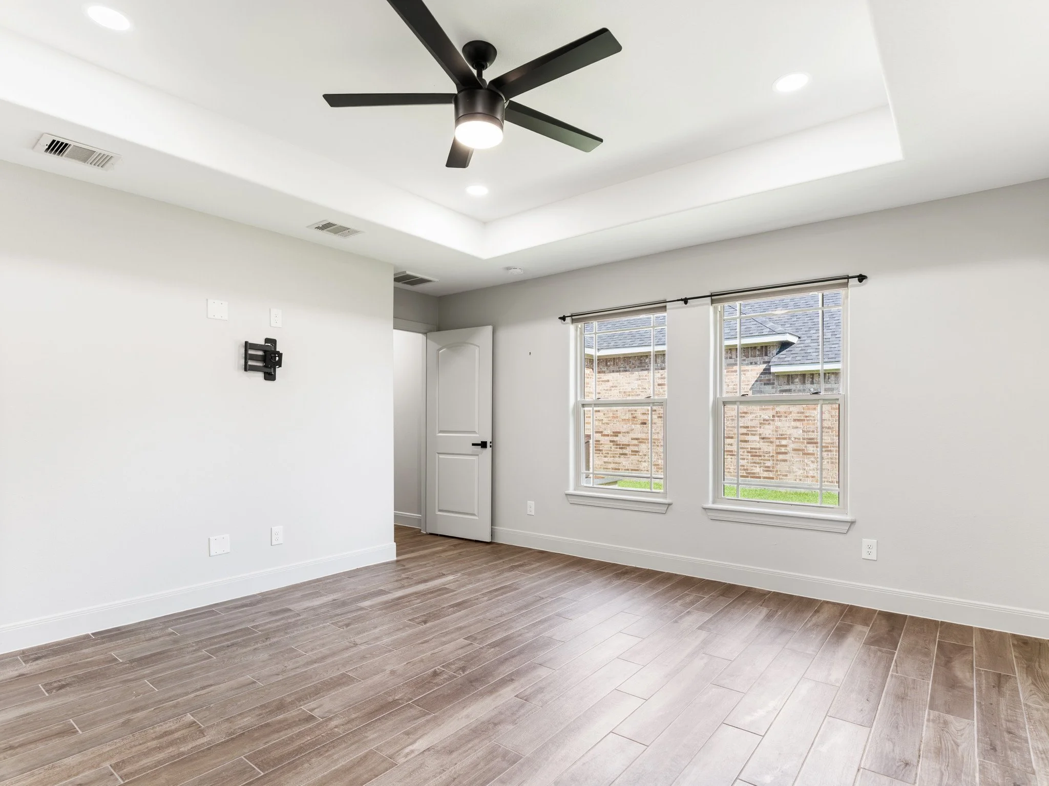 Empty room with wood flooring, white walls, two windows, a ceiling fan, and doors.