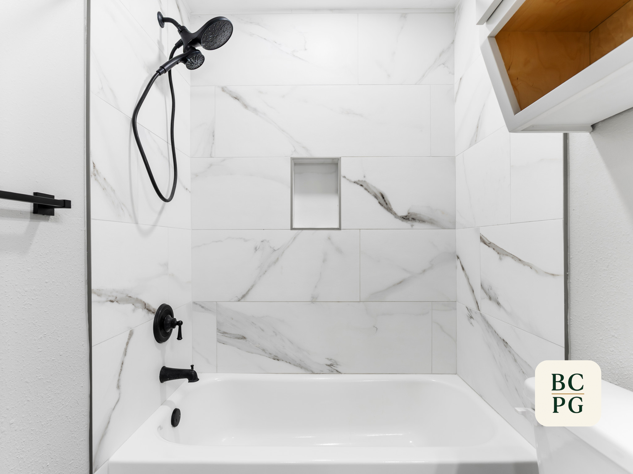 Top-down view of a modern shower stall with white marble tiles, a black showerhead, and fixtures, and a built-in shower niche with a wooden interior.