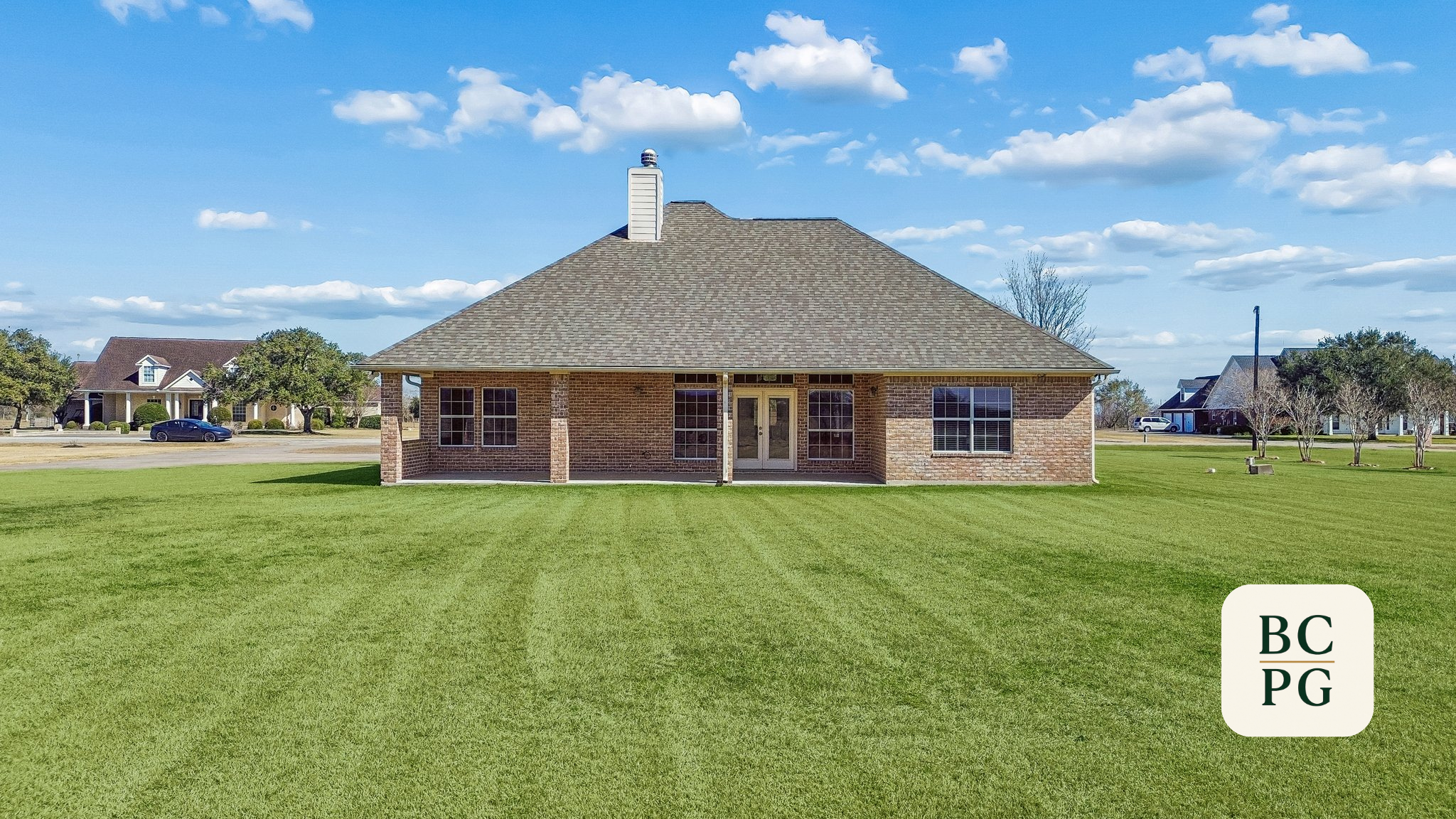 Brick house with a gable roof, multiple windows, a porch with columns, and a cloudy sky background. Green lawn in the foreground.