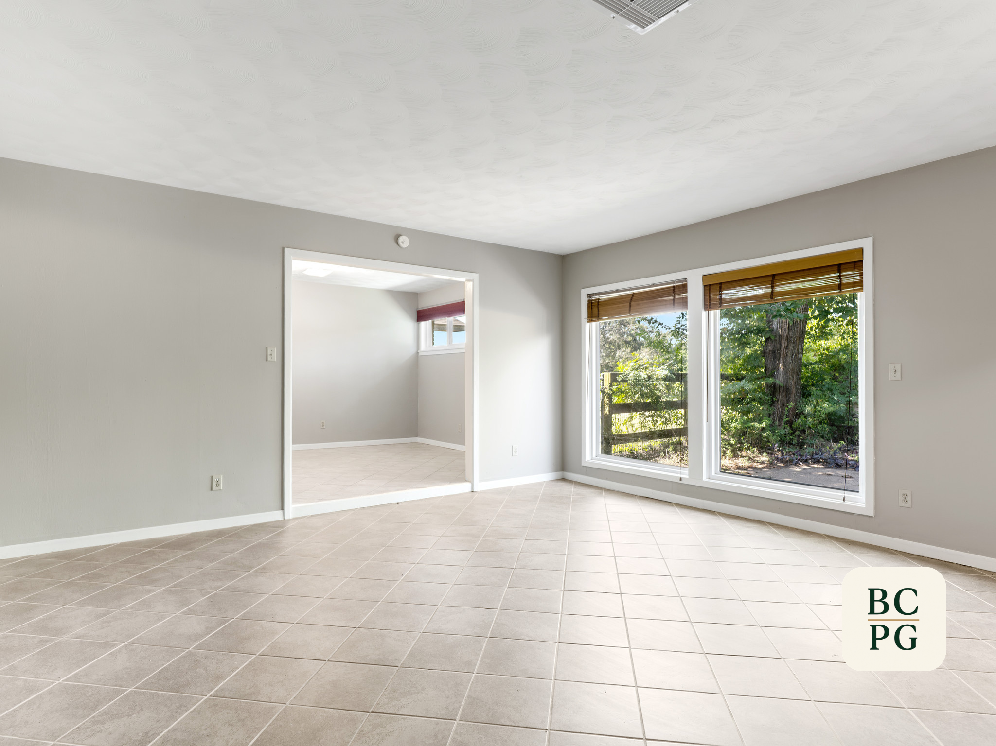 Empty room with large windows, beige tiled floor, gray walls, and a view of trees outside.