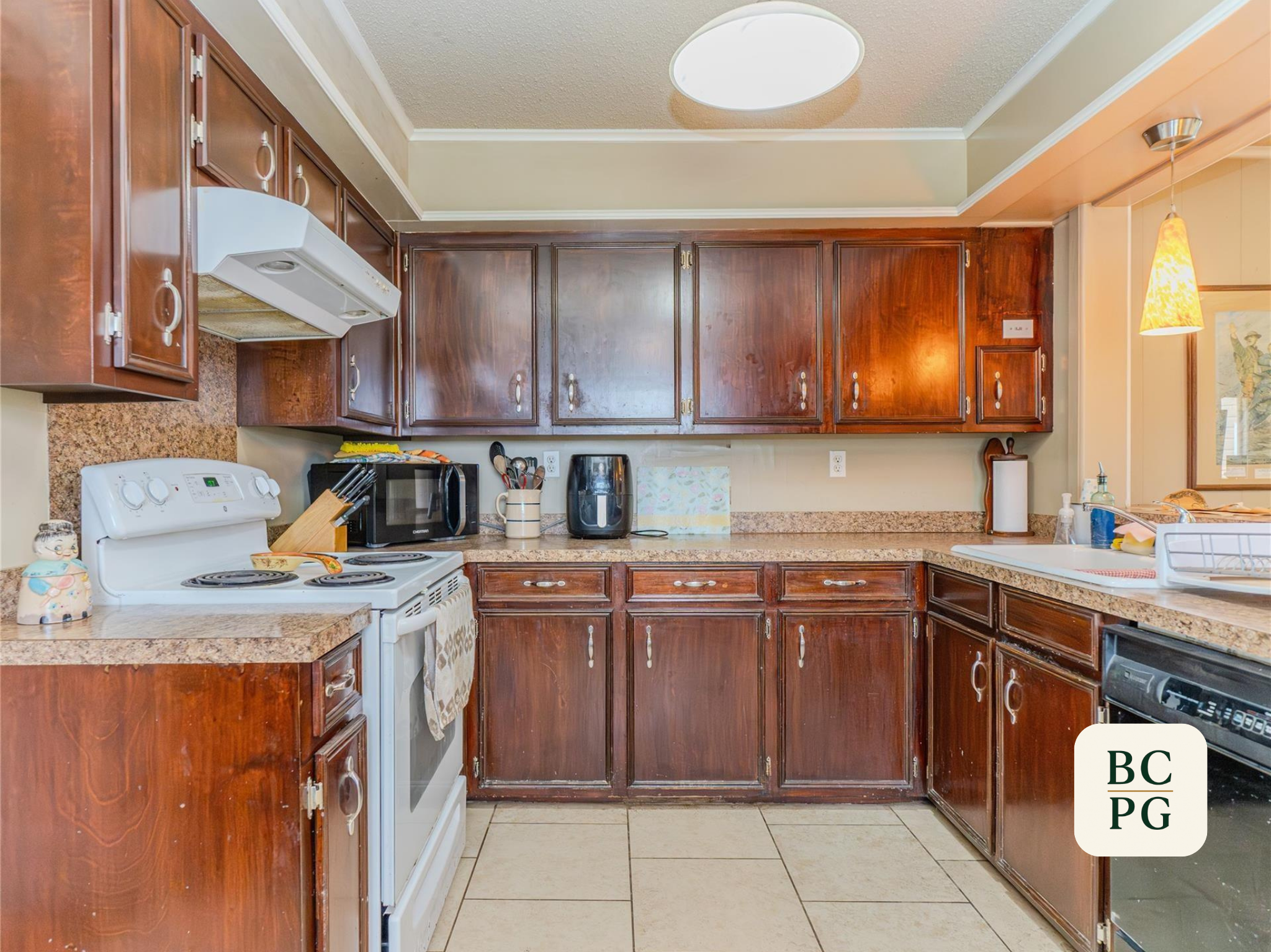A kitchen with dark wooden cabinets, white appliances, and various kitchen items on the countertops, including a microwave, toaster, and coffee maker.