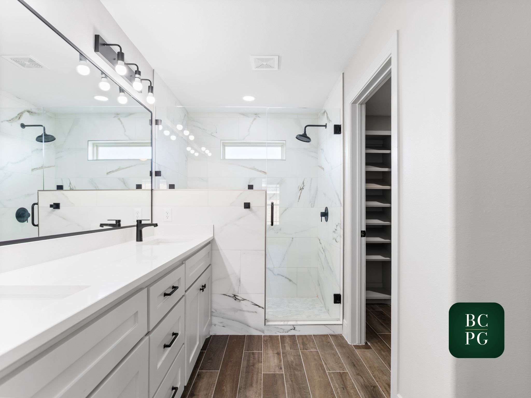 Modern bathroom with white vanity, black fixtures, marble shower walls, and wood-look tile flooring.