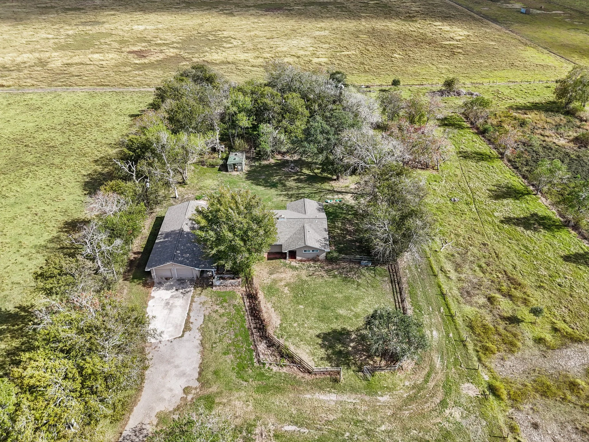Aerial view of a house with a driveway, surrounded by trees and open fields.