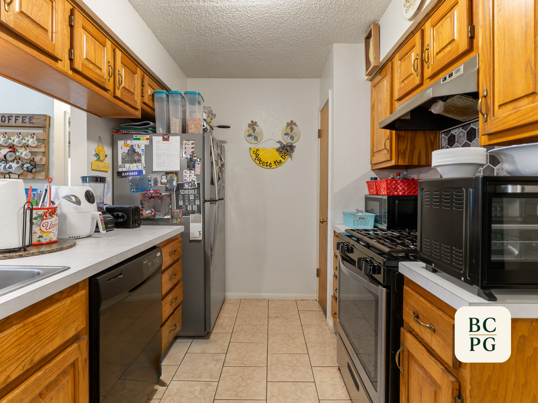 A kitchen with wooden cabinets, a refrigerator covered with magnets and photos, a microwave on a white counter, a stove, and various kitchen utensils and decorations.