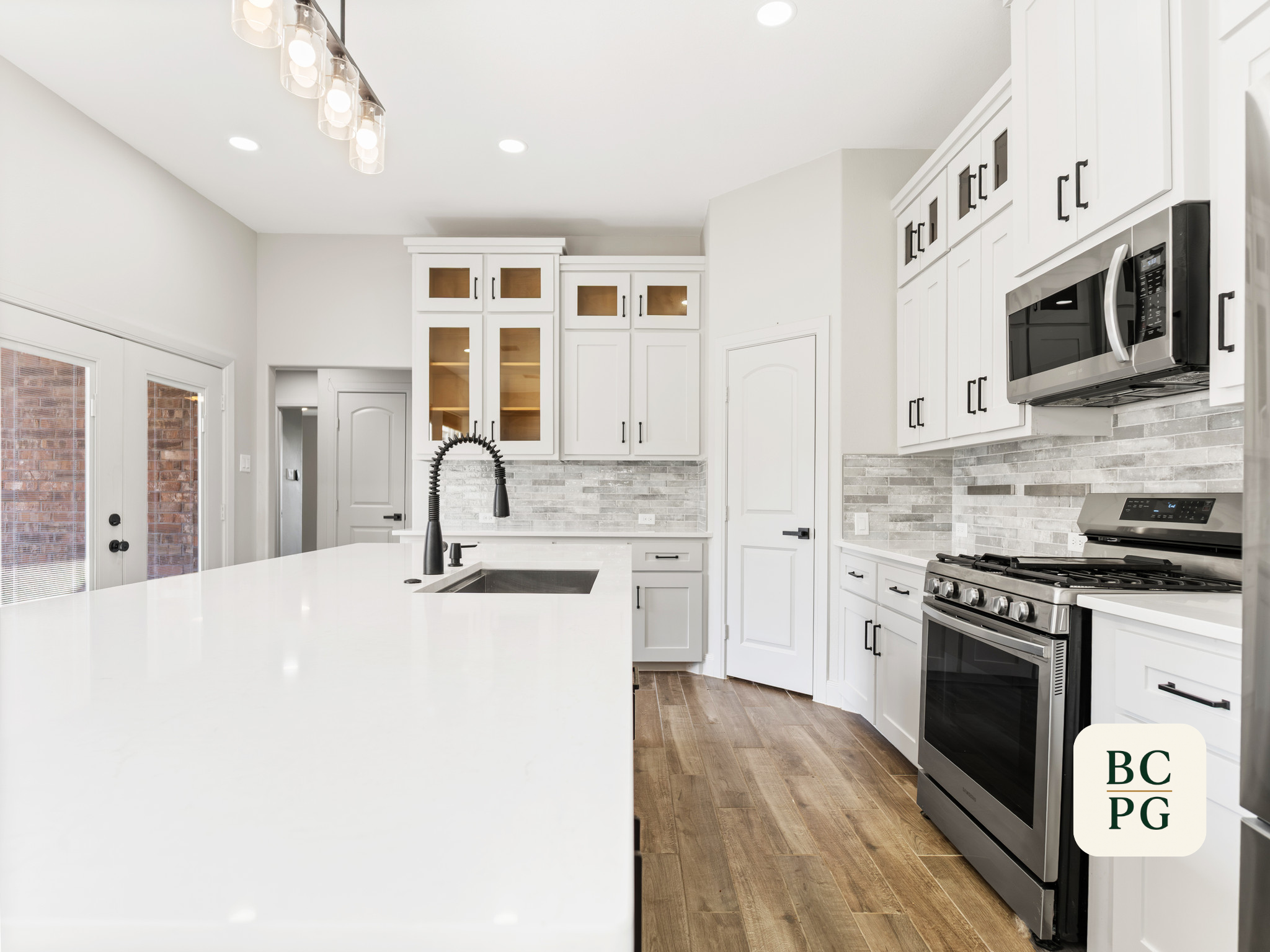 Modern kitchen with white cabinets, black hardware, stainless steel appliances, a black faucet, and wood flooring.