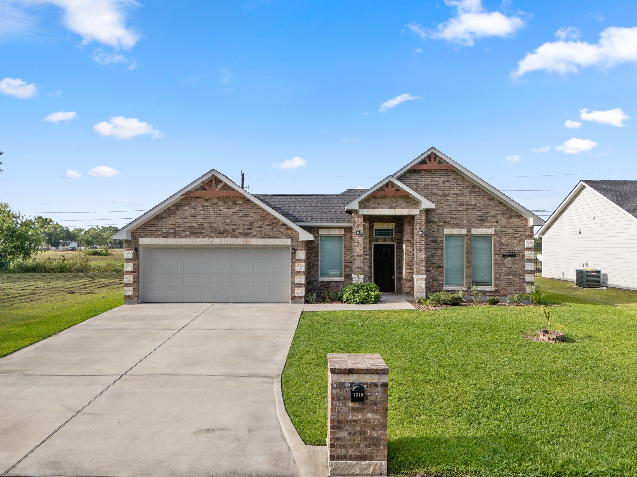 A brick house with a garage, a front yard with green grass, and a sidewalk leading to the front door, under a blue sky with some clouds.
