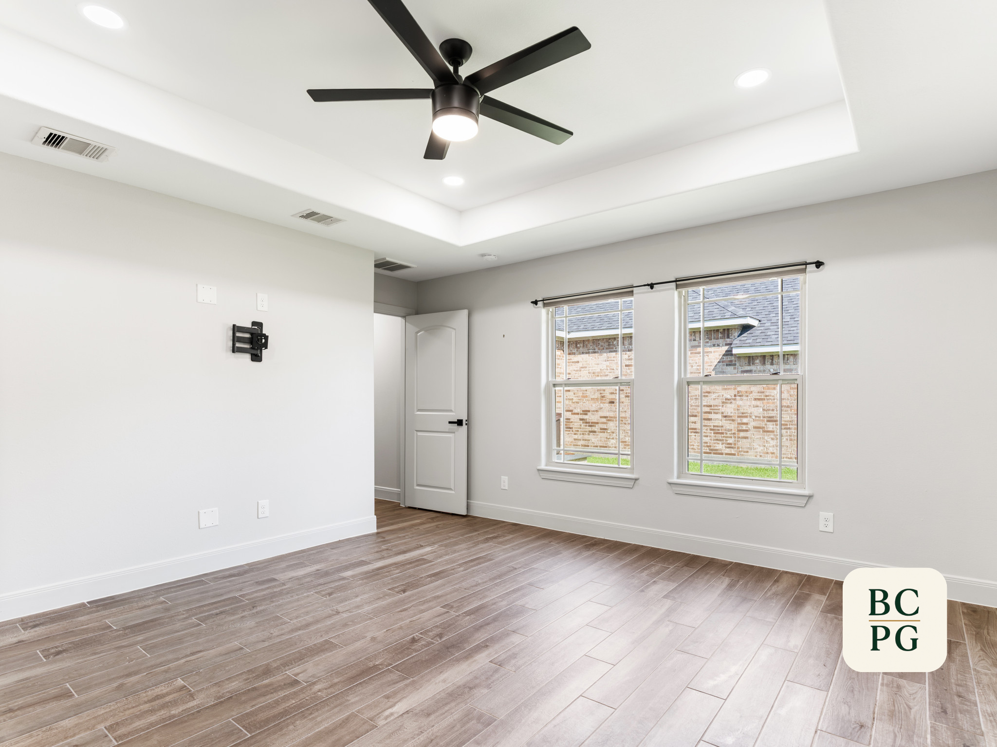 Empty room with hardwood floors, white walls, large windows, and a ceiling fan with lights.