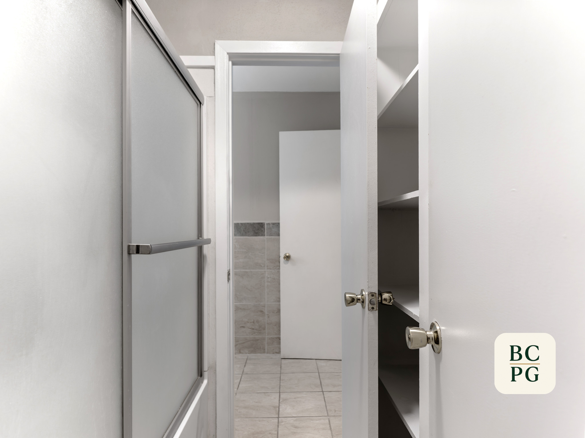 View of an open bathroom stall with a white door and a tiled shower in the background.