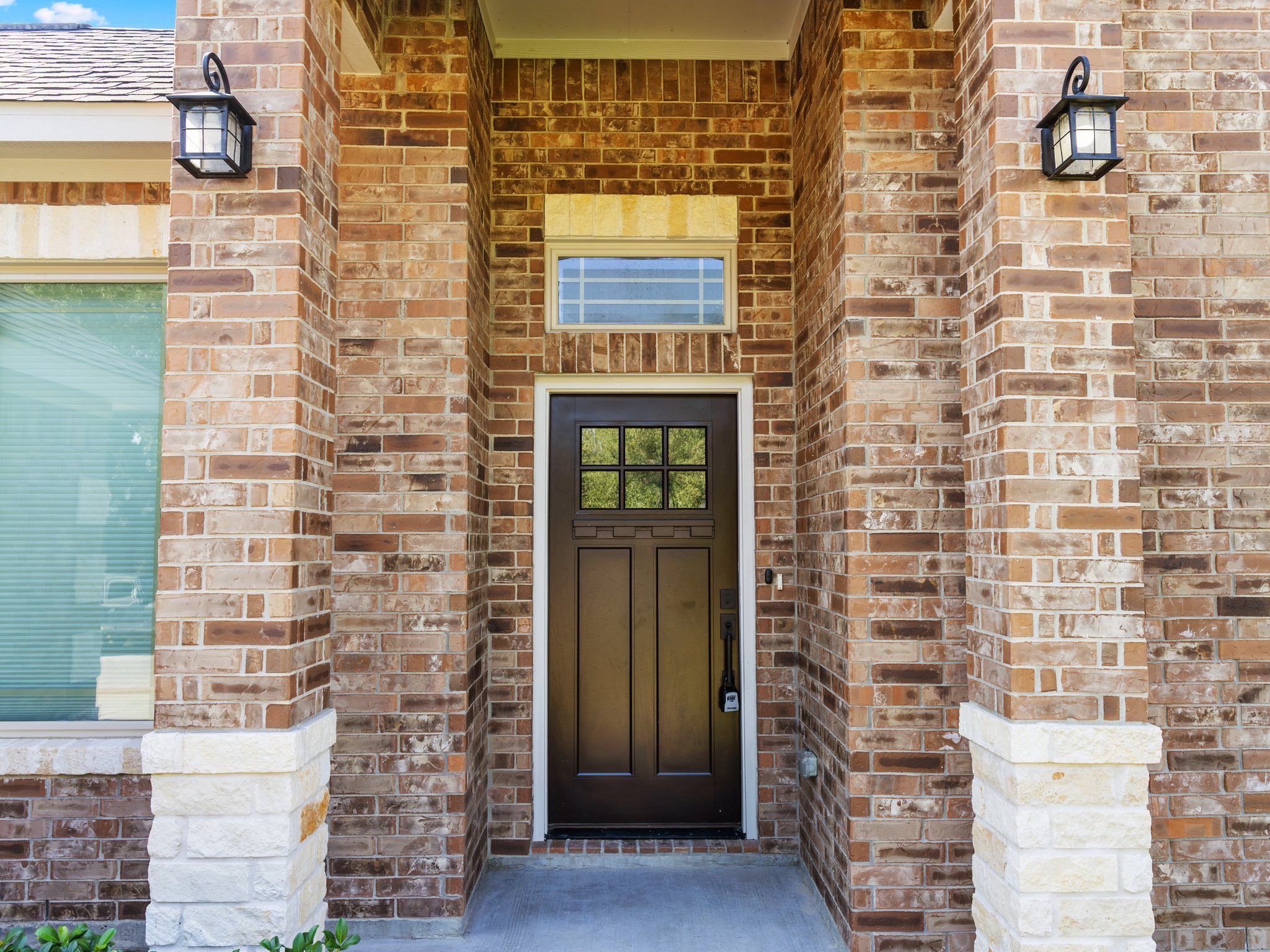 Brick house front entrance with a black door, two small windows above, and mounted black lanterns on each side of the brick walls.