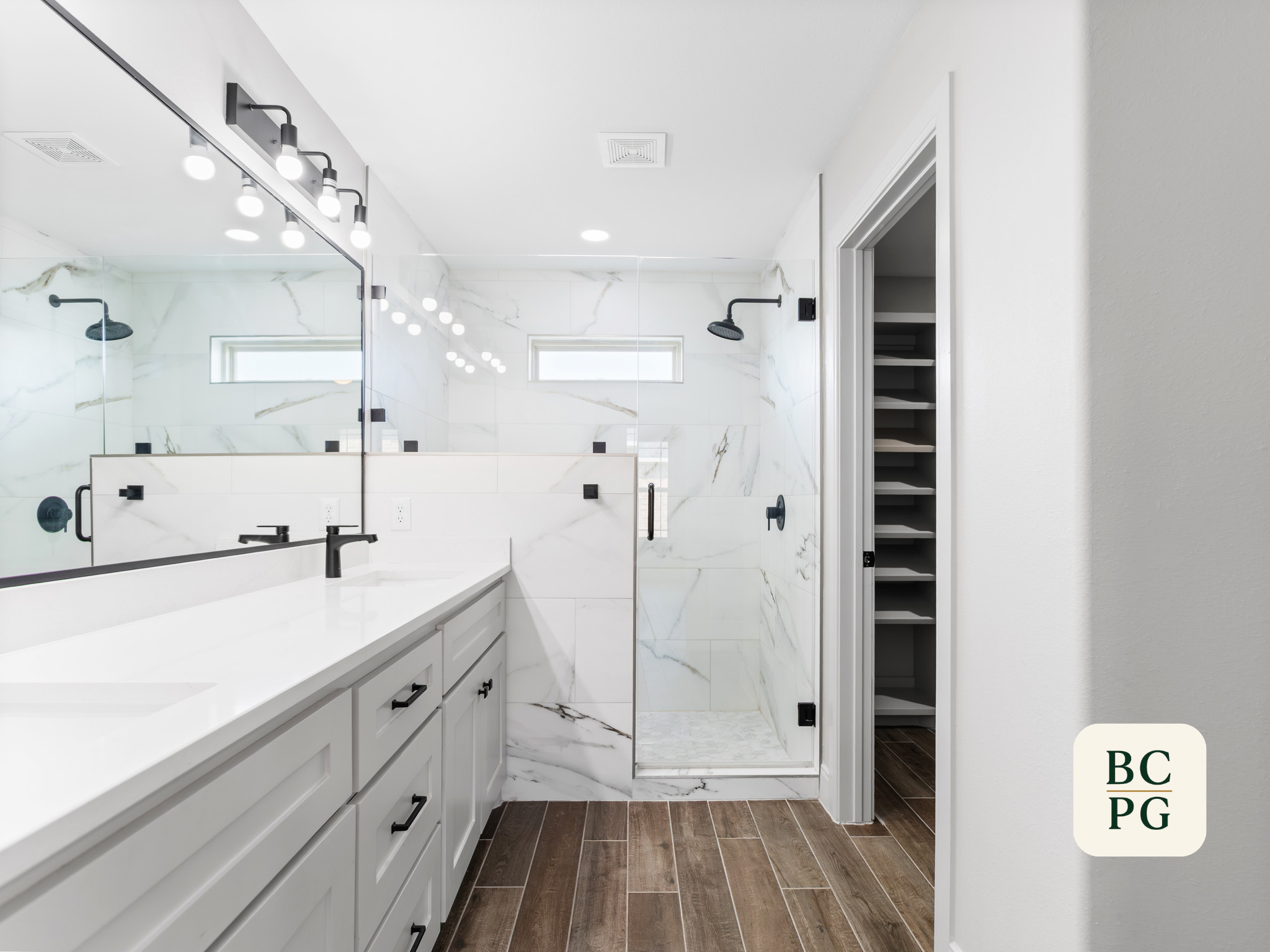 Modern white bathroom with a large mirror, black fixtures, marble shower walls, and a walk-in shower with a glass door.