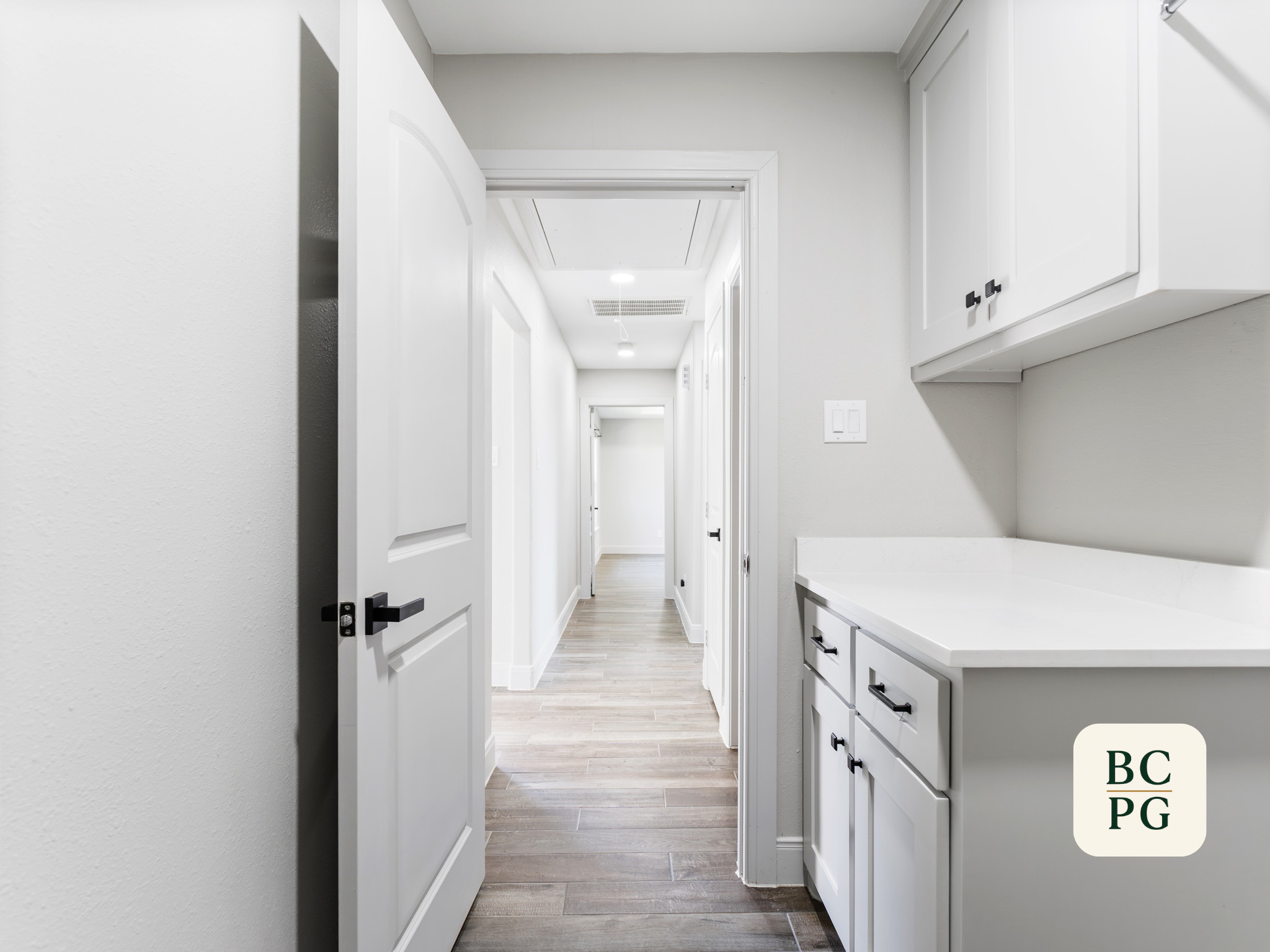 A bright, white hallway with white doors, cabinets, and trim, featuring a wooden floor and ceiling lights.