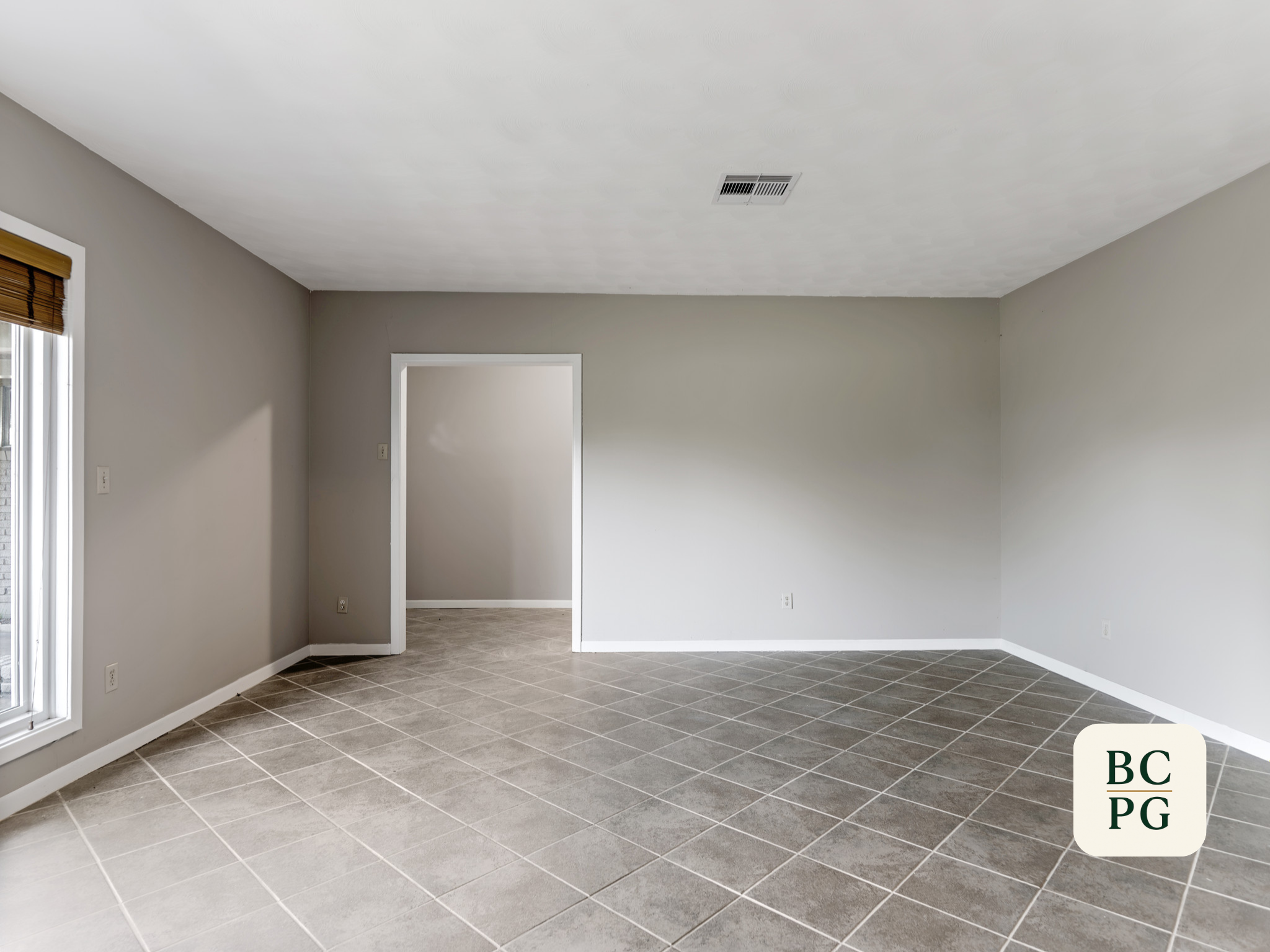 Empty living room with gray walls, beige carpet, and tiled floor, with window and doorway.