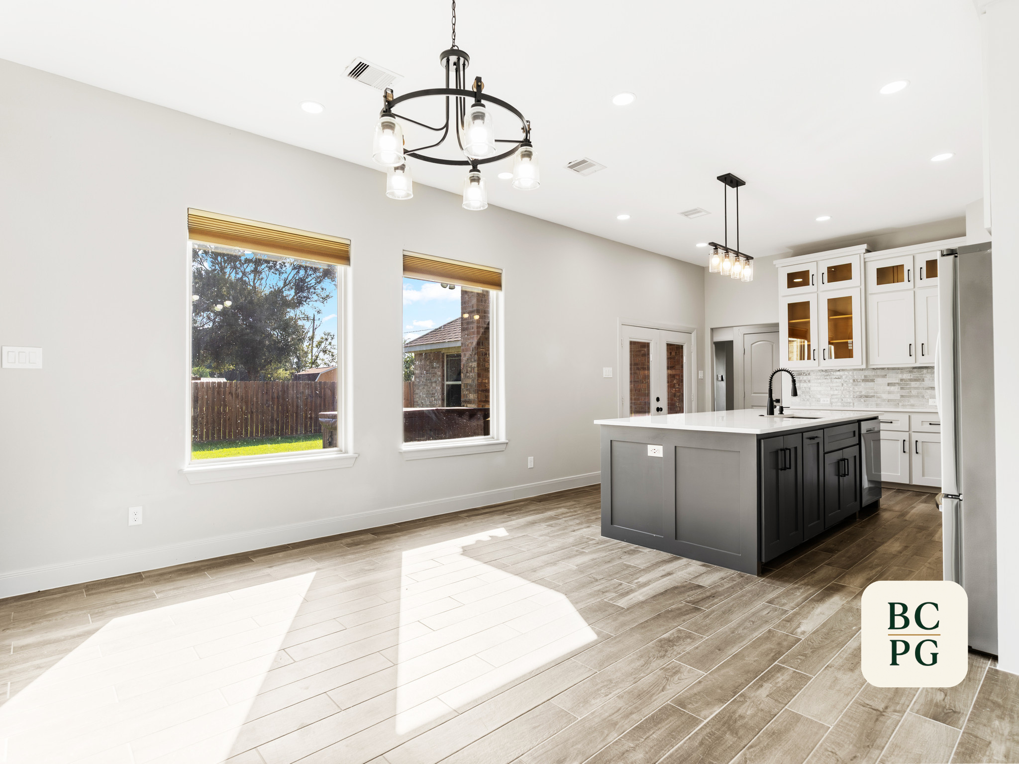 Modern kitchen with white cabinets, island with black base, pendant lighting, and large windows with view of backyard.