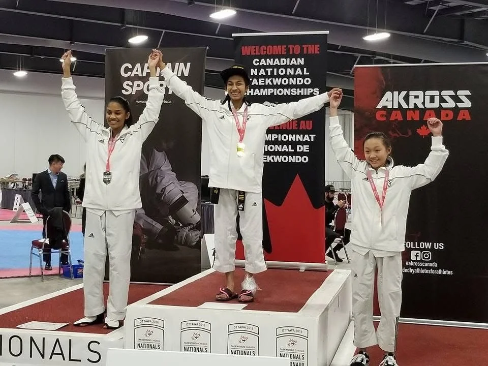A man with dark curly hair and a beard, wearing clear-framed glasses and a dark green sweater, looking to the side in an indoor setting.