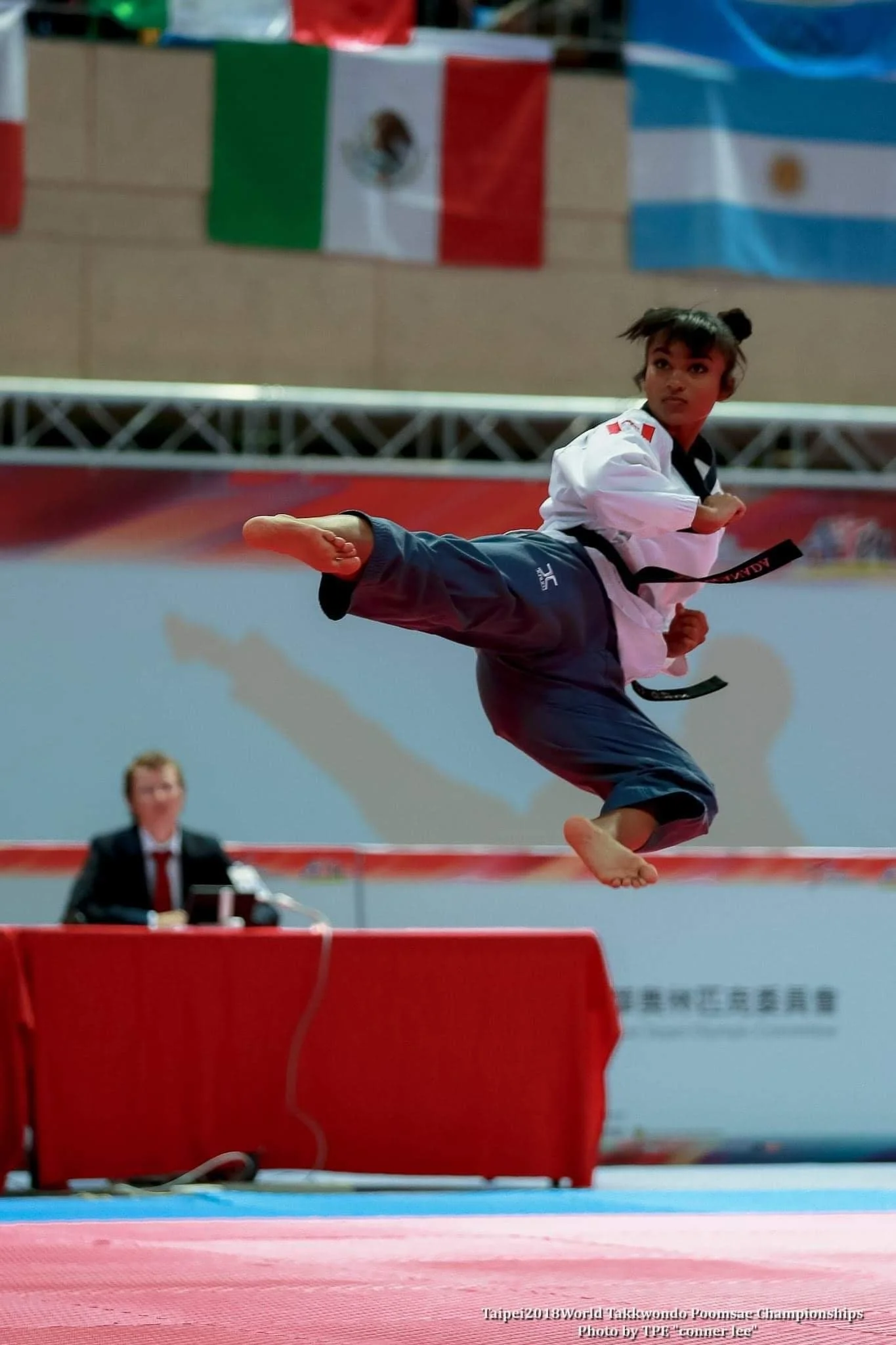 Smiling person with curly hair and glasses, wearing a striped top and necklaces.