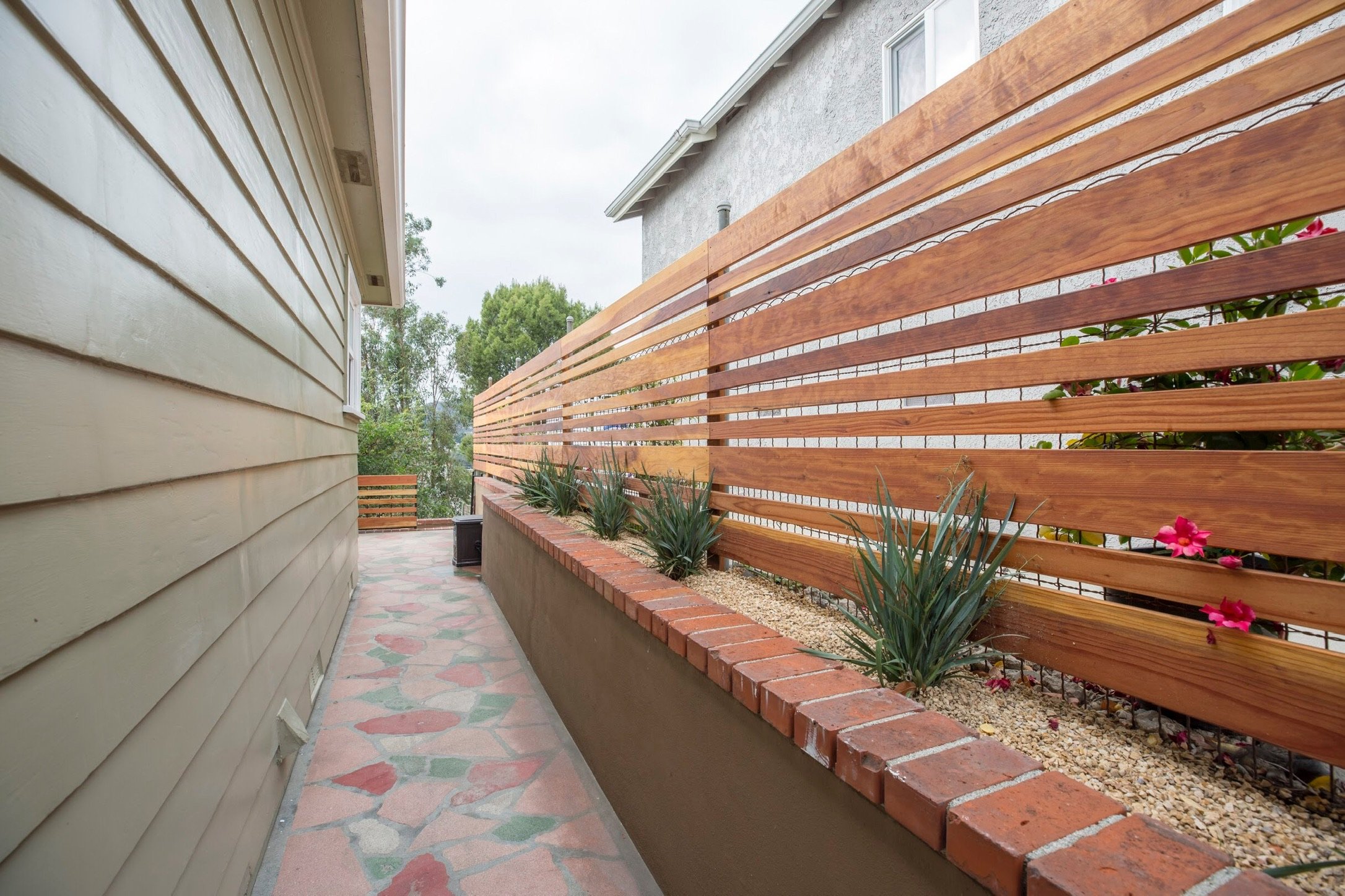 Patio walkway with wood fence, brick planter, and plants