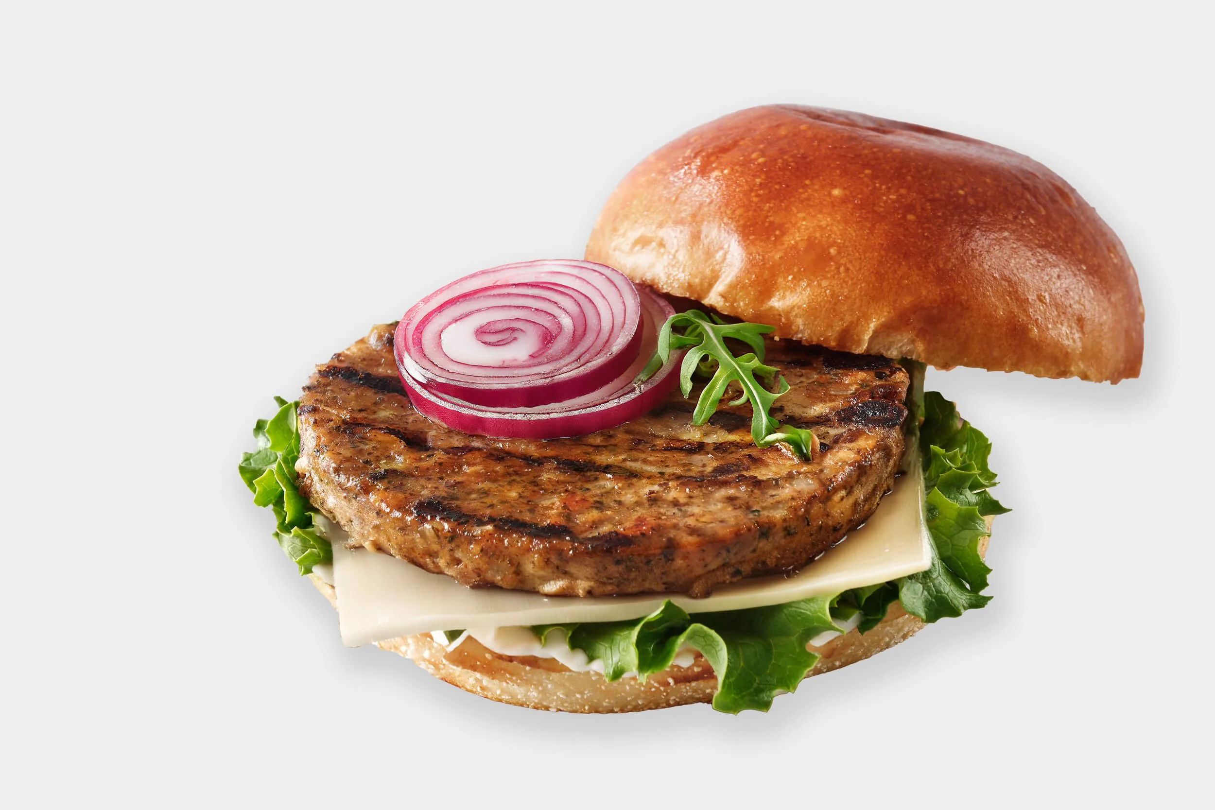 Hamburger with grilled patty, sliced red onion, lettuce, cheese, and a toasted bun on a white background.