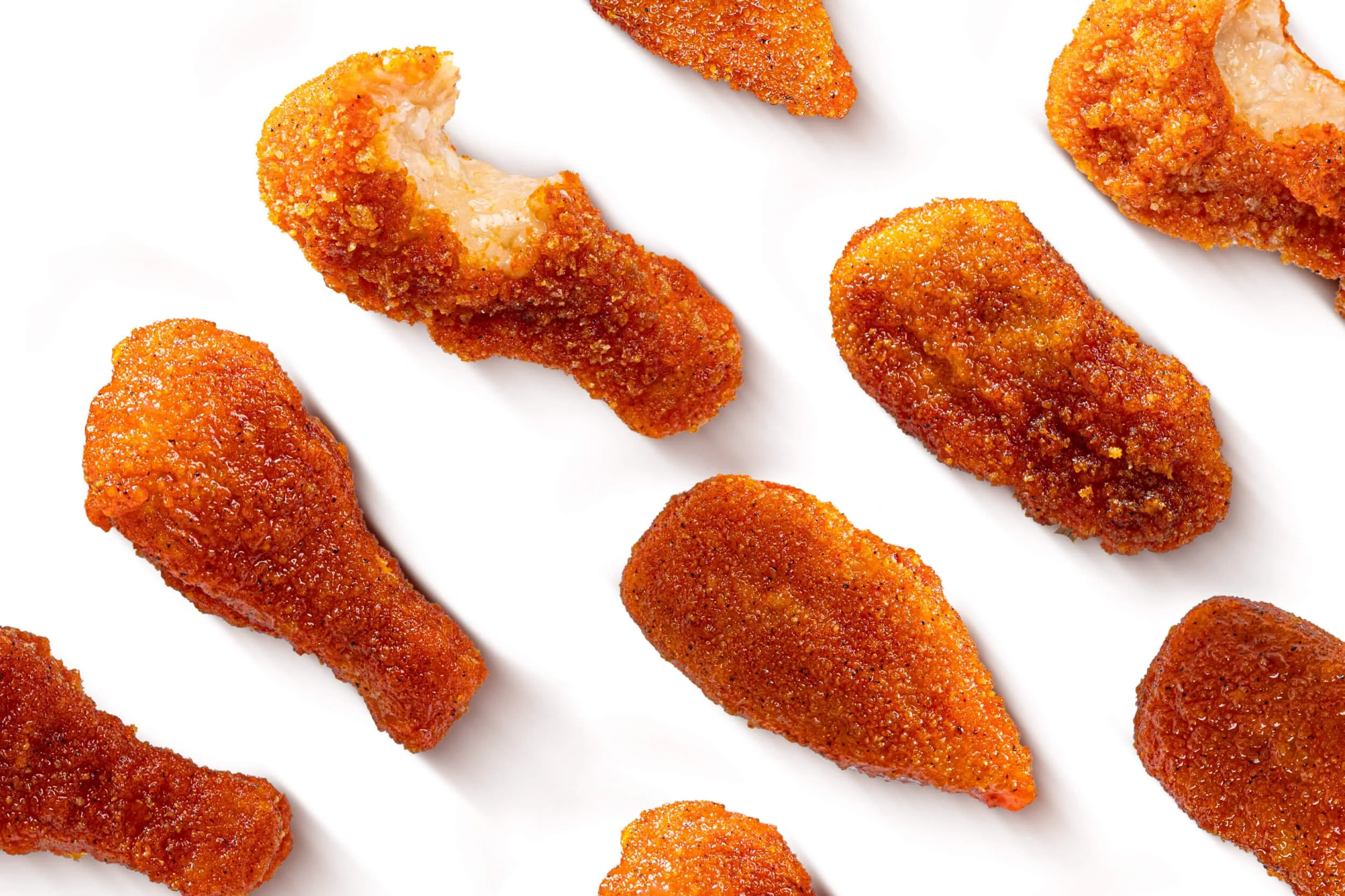 Several pieces of crispy, breaded, cooked chicken drumsticks and fillets on a white background.