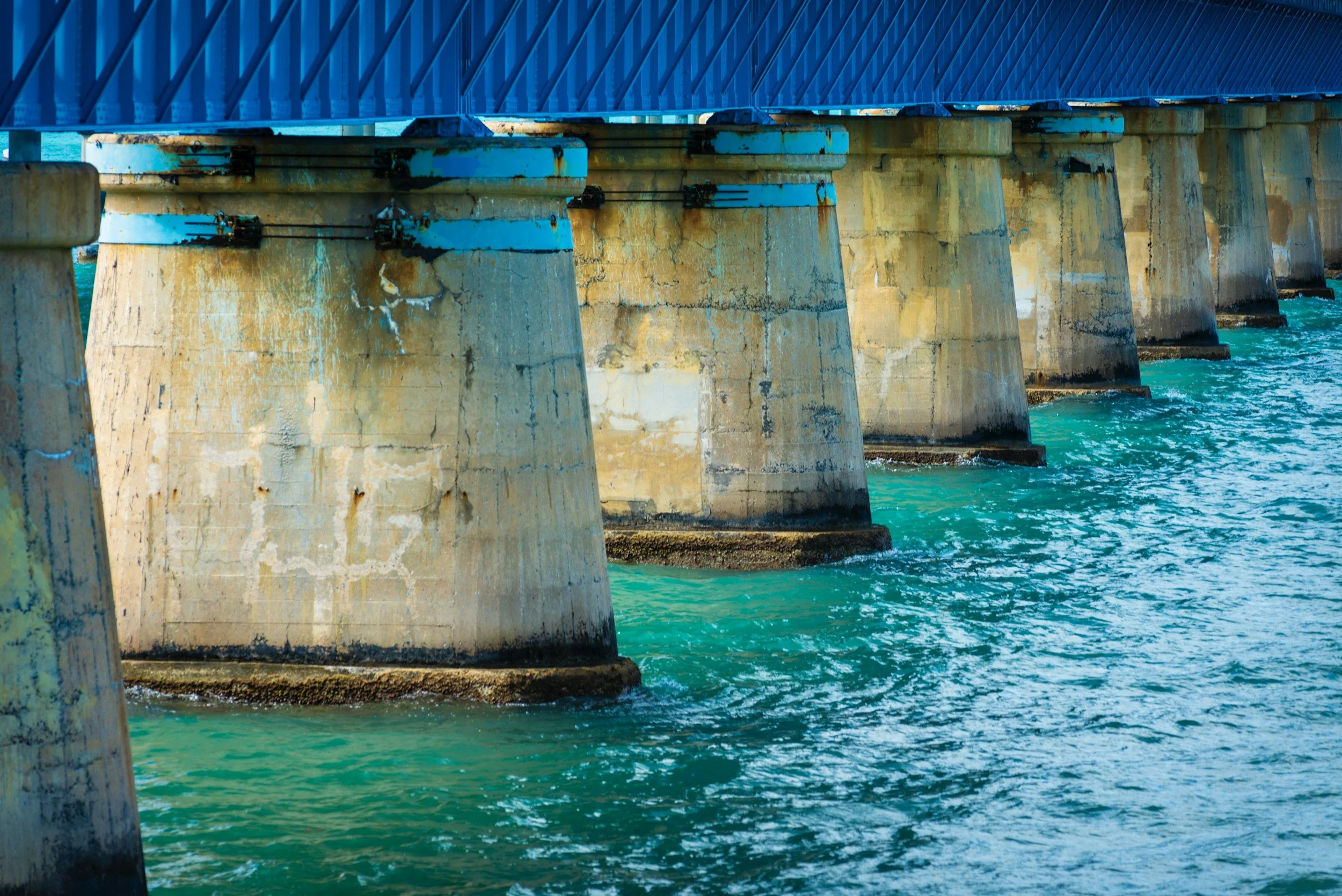 View of a bridge supported by multiple concrete pillars extending into the turquoise water below.