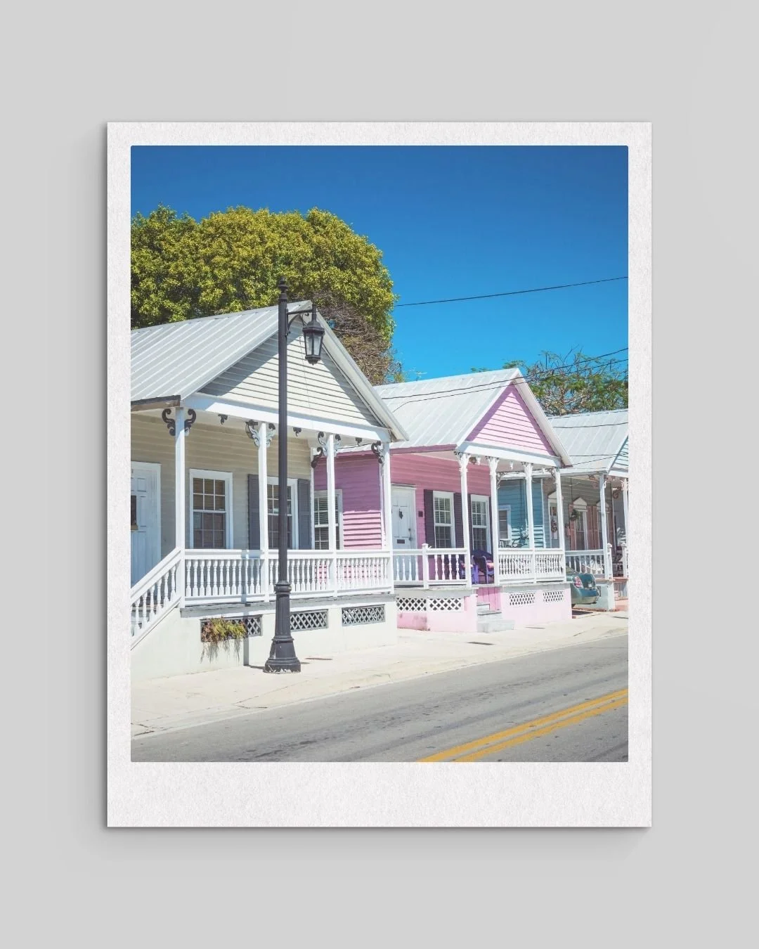Colorful houses with porches along a street, a streetlamp, and a tree in the background under a clear blue sky.