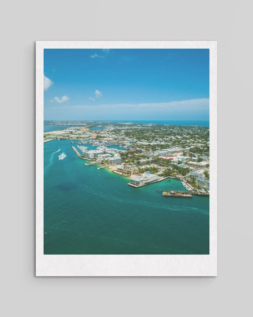 Aerial view of a coastal city with buildings, docks, and boats on a clear day with blue skies.