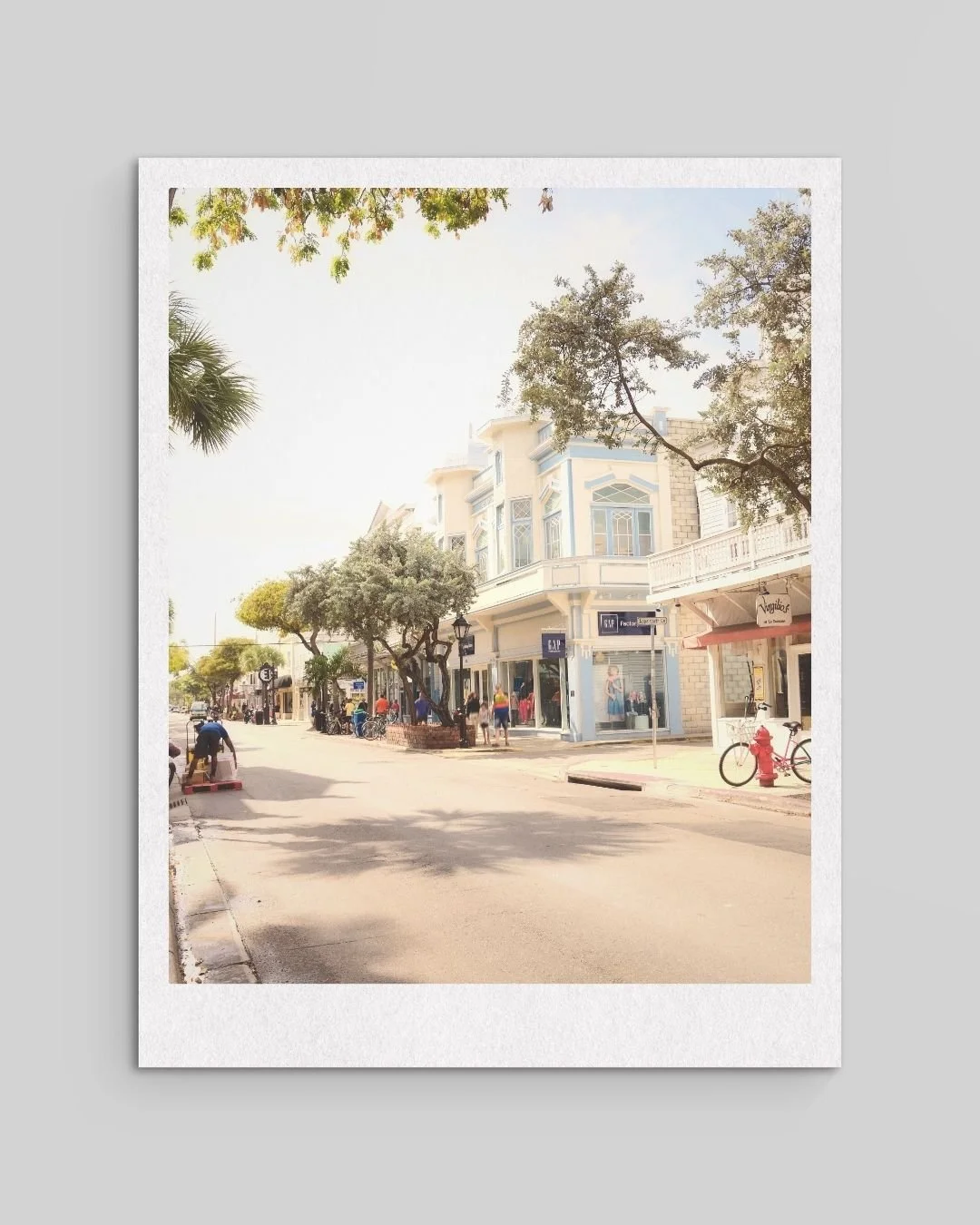 A street view with trees, a building with a clothing store, bicycles, and pedestrians on a sunny day.