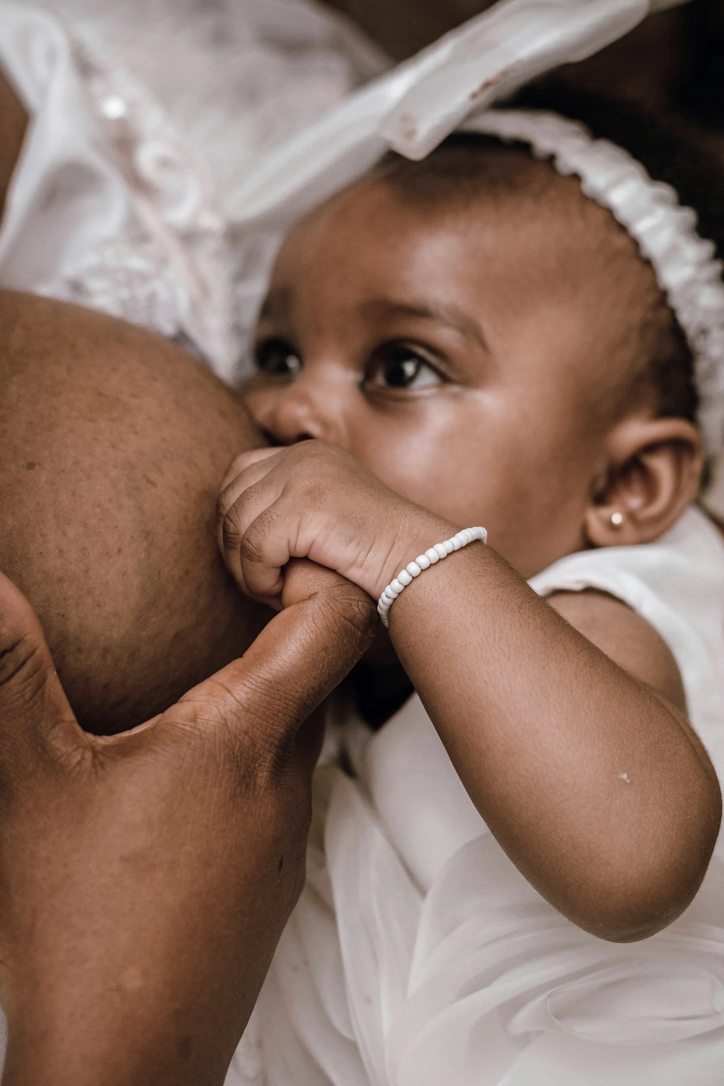 A young child with a white beaded bracelet is breastfeeding, shown close-up with the child's face and hand visible.