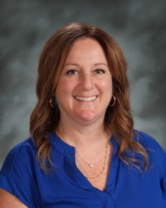 A school emblem with a shield divided into four sections: a cross and crown, a female saint or religious figure, a scroll, and a dove. Below the shield, a banner reads "Adora Disce Serve 1983." Beneath the emblem, bold text says "Coming Soon."