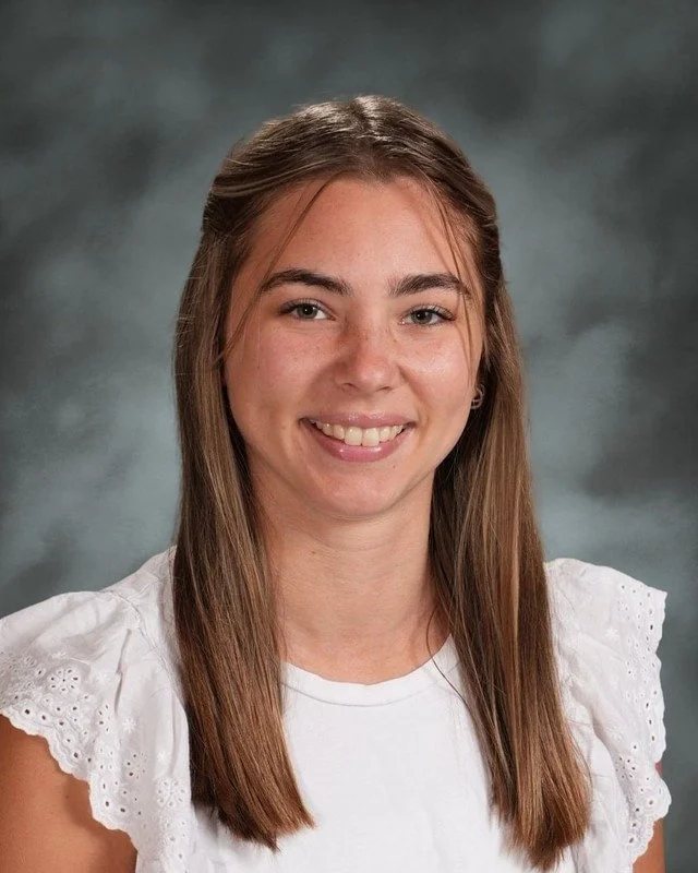 A crest shield with religious symbols, a haloed woman, a rolled scroll, and a dove, with a banner reading "Adora Disce Serve" and the year 1983, and the text "Coming Soon" below.