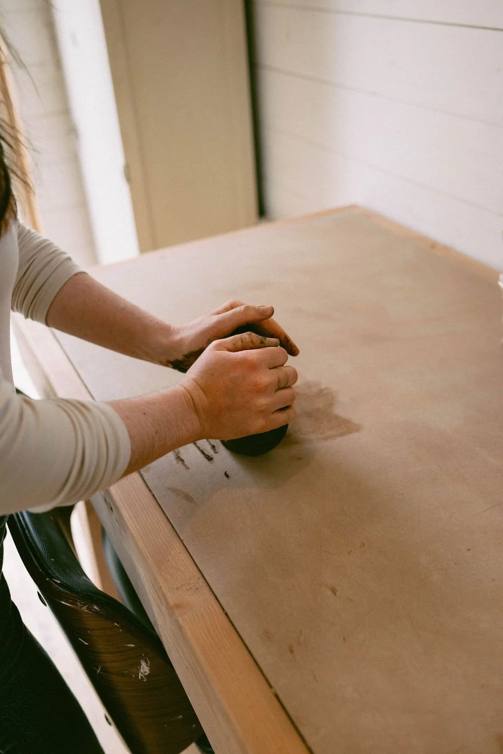 Claire Lemp Ceramics. Person kneading clay on a wooden work surface in a well-lit room.