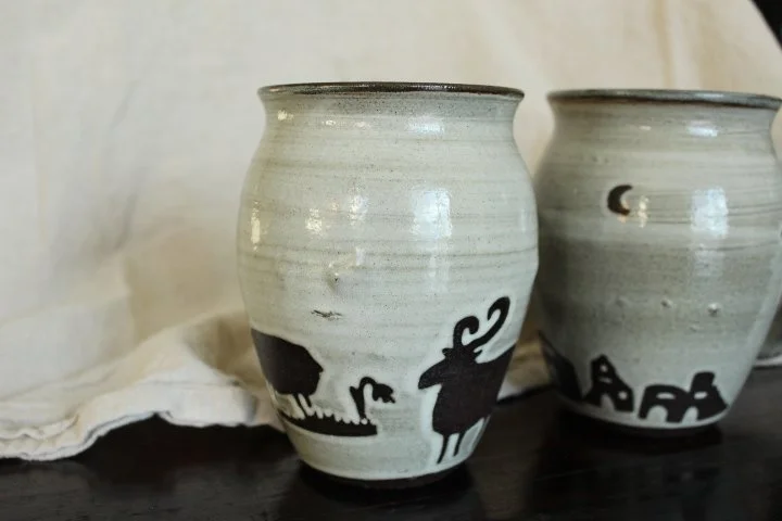 Claire Lemp Ceramics. Bozeman, MT Potter, pottery. Montana Ceramics, ceramicist. Made In Montana. Ceramic vases with black skull and animal designs on a dark surface.