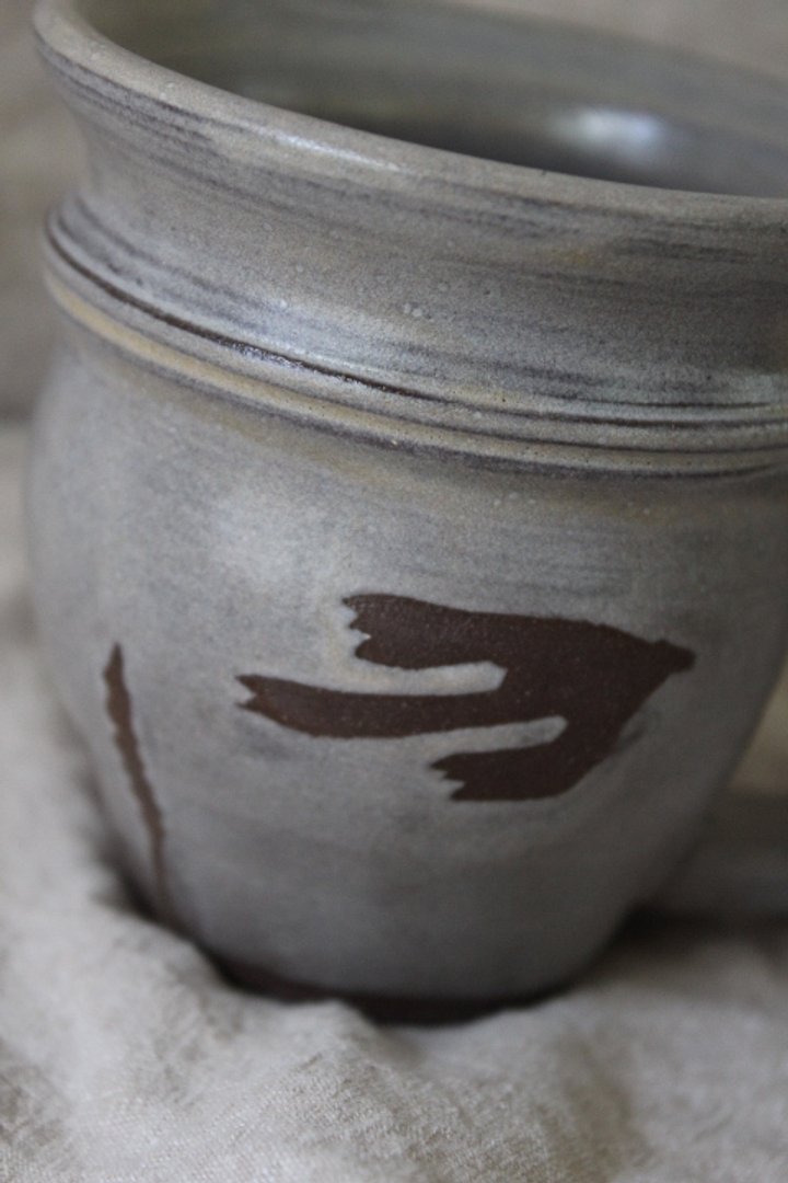 Claire Lemp Ceramics. Bozeman, MT Potter, pottery.  Close-up of a gray ceramic vase with dark brown decorative patterns, sitting on a light-colored cloth.