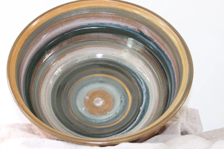 Claire Lemp Ceramics. Bozeman, MT Potter, pottery.  Top view of a large ceramic bowl with multicolored swirl patterns inside, placed on a white surface with a cloth underneath.
