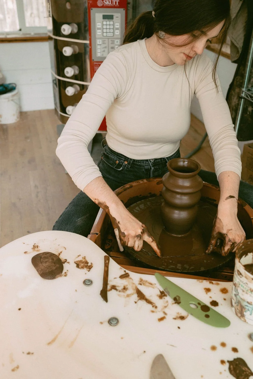 Claire Lemp Ceramics. Bozeman, MT Potter, pottery. A woman is creating a pottery piece on a pottery wheel in a studio, surrounded by clay and tools.