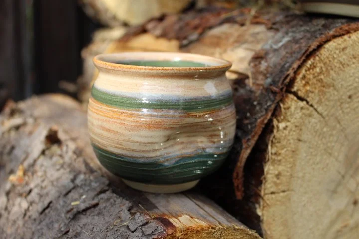 Claire Lemp Ceramics. Bozeman, MT Potter, pottery.  A ceramic bowl with green, beige, and brown swirl pattern placed on chopped firewood.