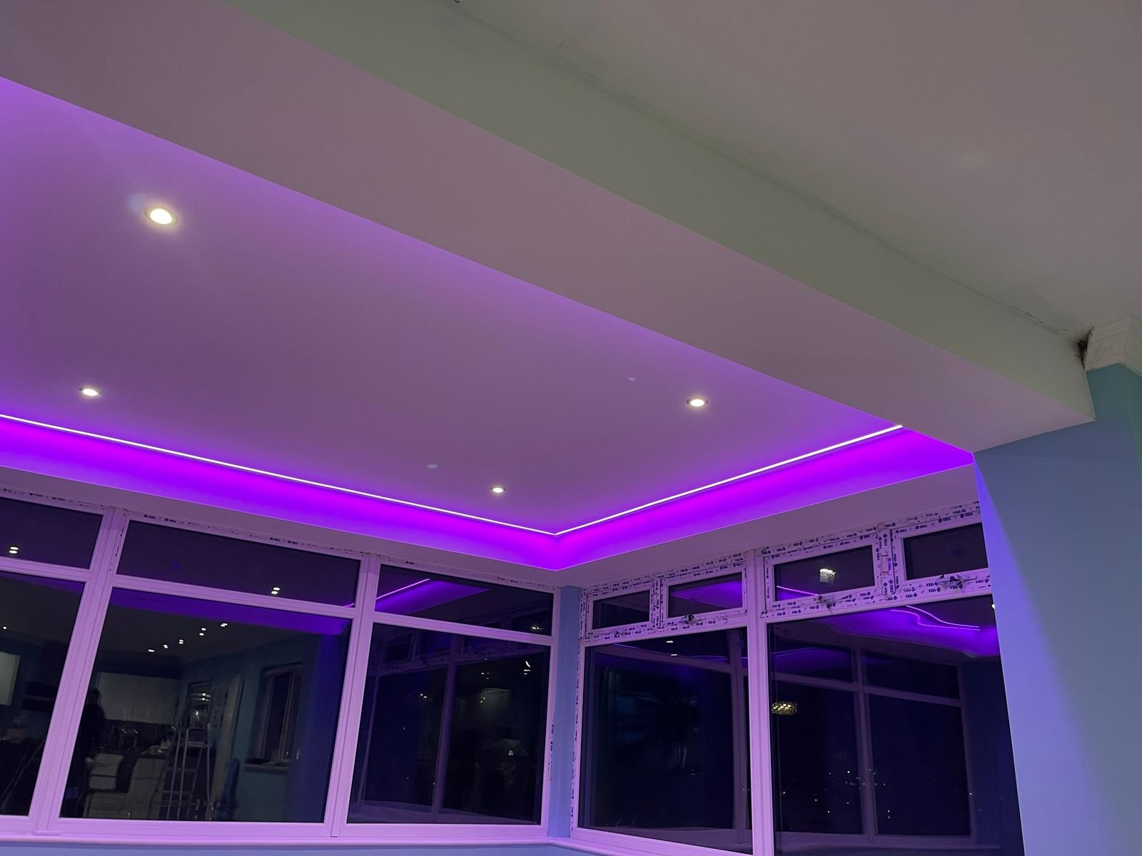 Interior of a room with large windows and purple LED ceiling lights.