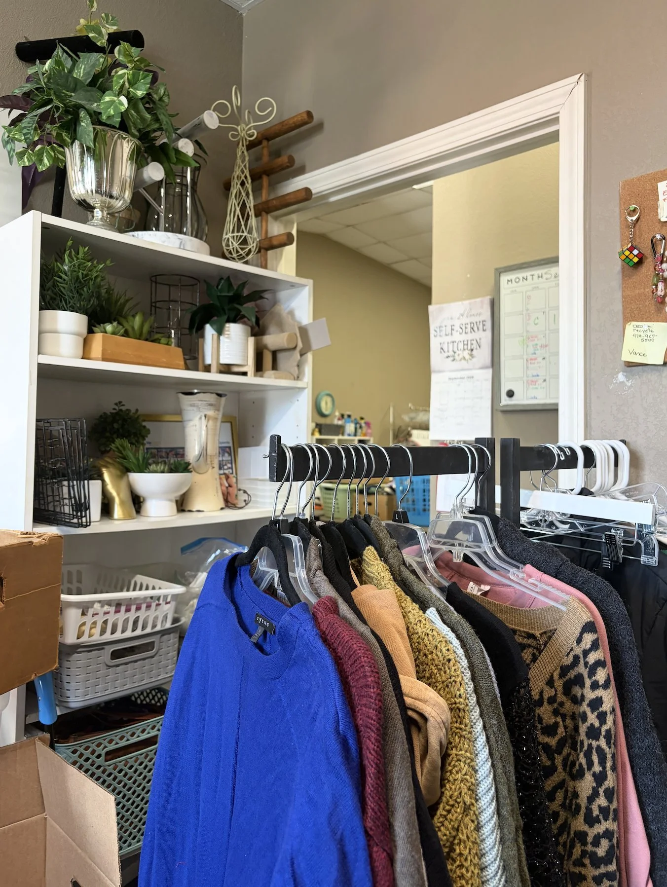 Sweaters hang on a rack beside a shelf of donated plants and home decor inside the expanded UpStart Thrift store in Farmington, Arkansas