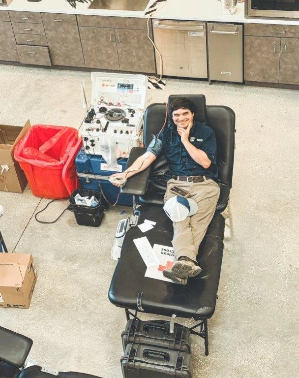 A man in a medical uniform donating blood while lying on a hospital bed in a clinical setting.