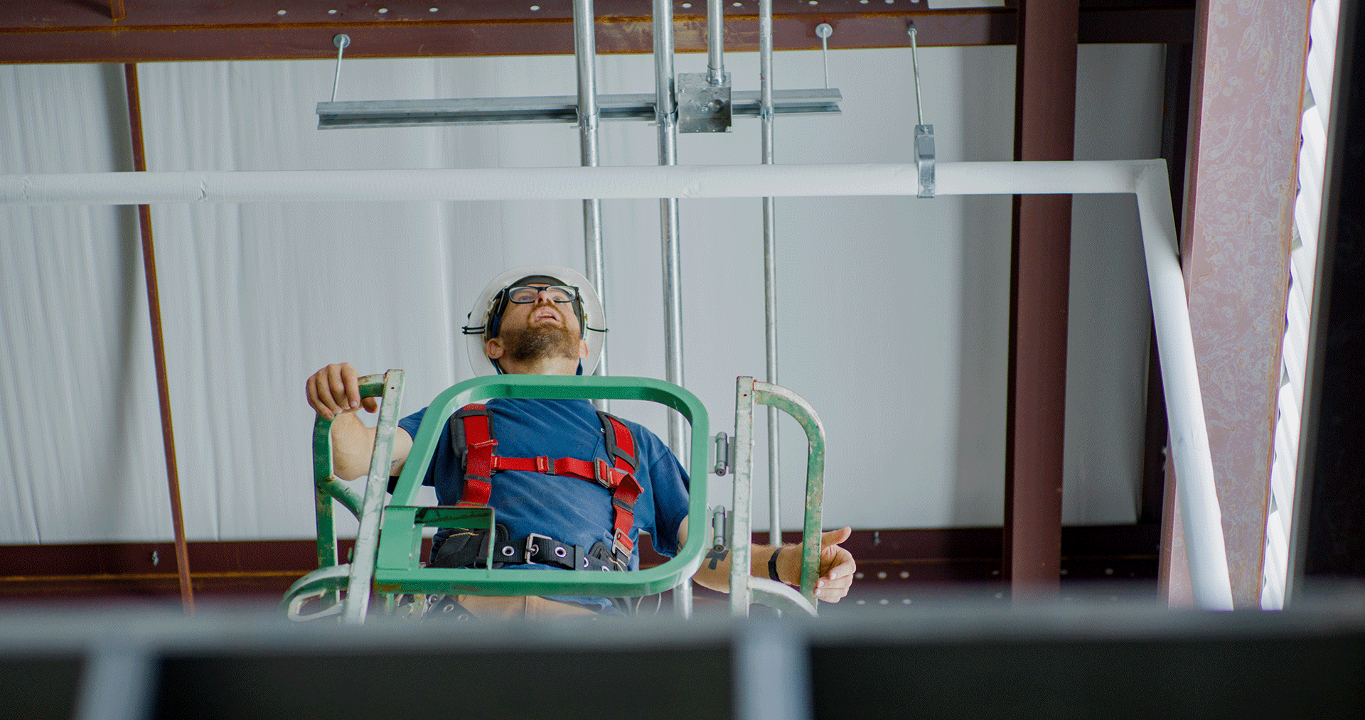 A man lying on a medical lift in a construction setting, wearing glasses and a helmet, with safety harnesses attached.