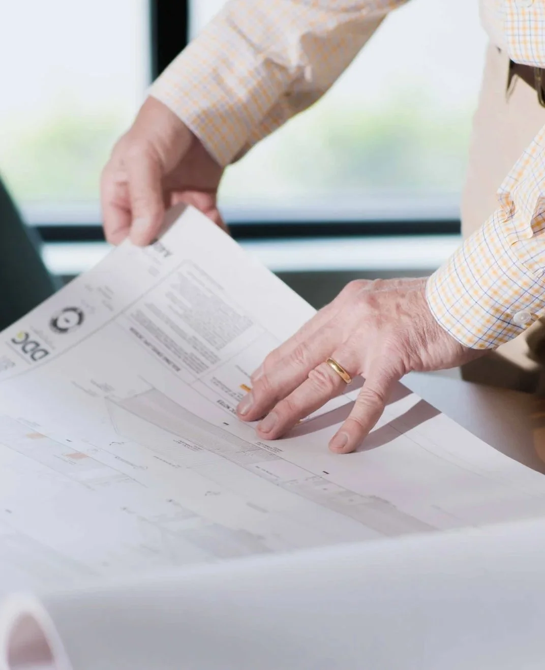 Person reviewing architectural blueprints or plans on a table near a window.