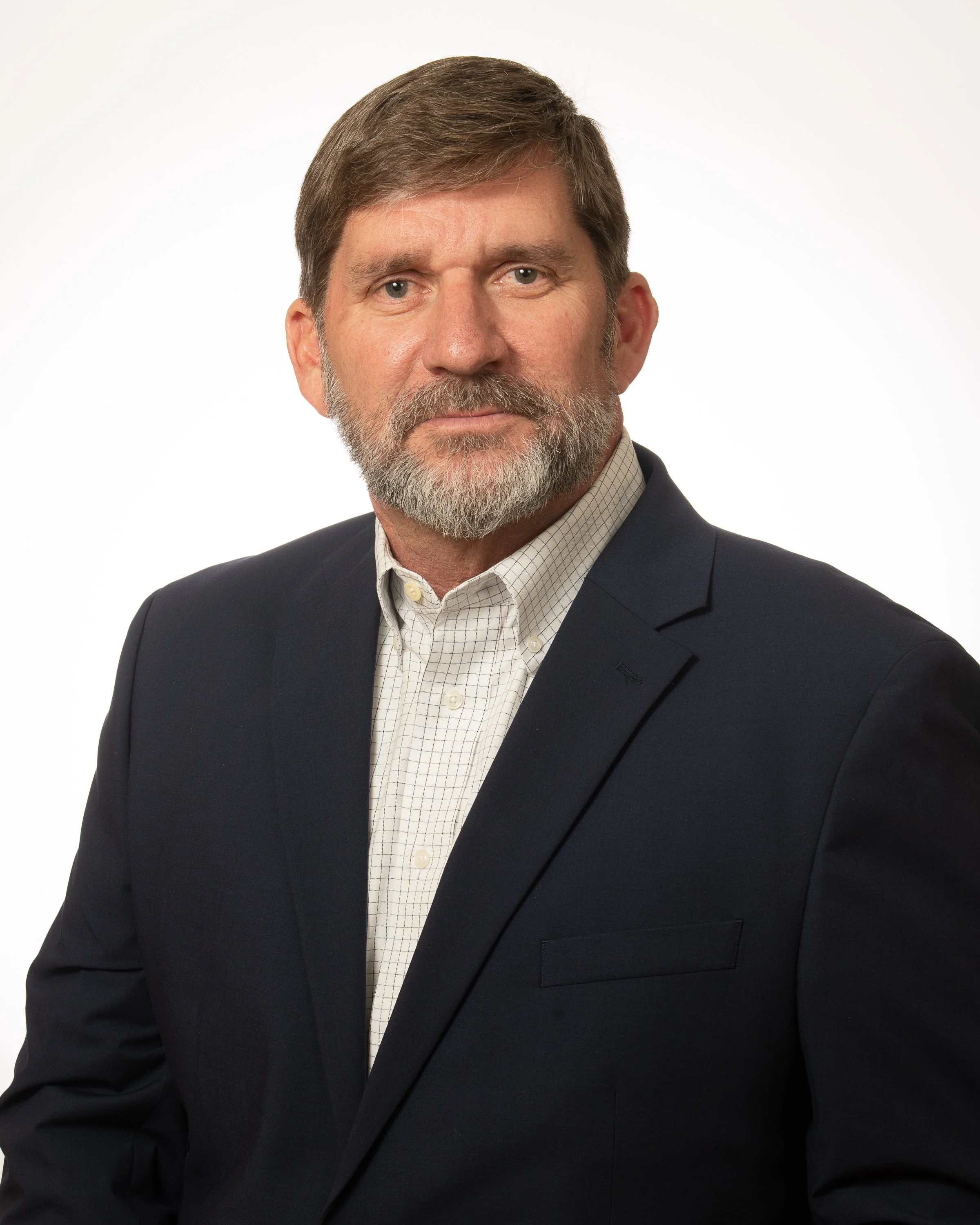 A middle-aged man with brown hair and a beard, wearing a dark button-down shirt with a small red logo, posing against a plain white background.