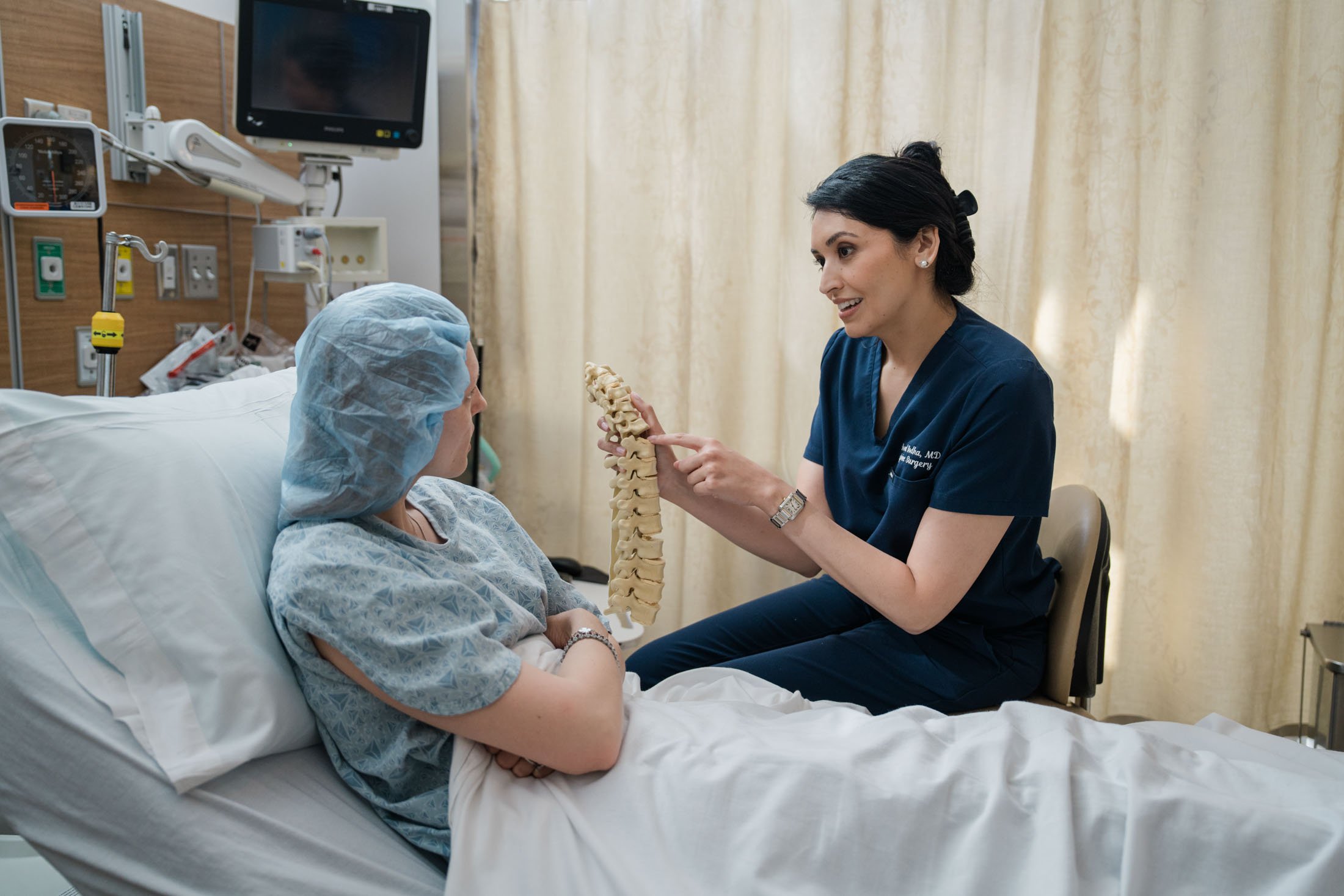 A female doctor explaining a spine model to a patient in a hospital room.