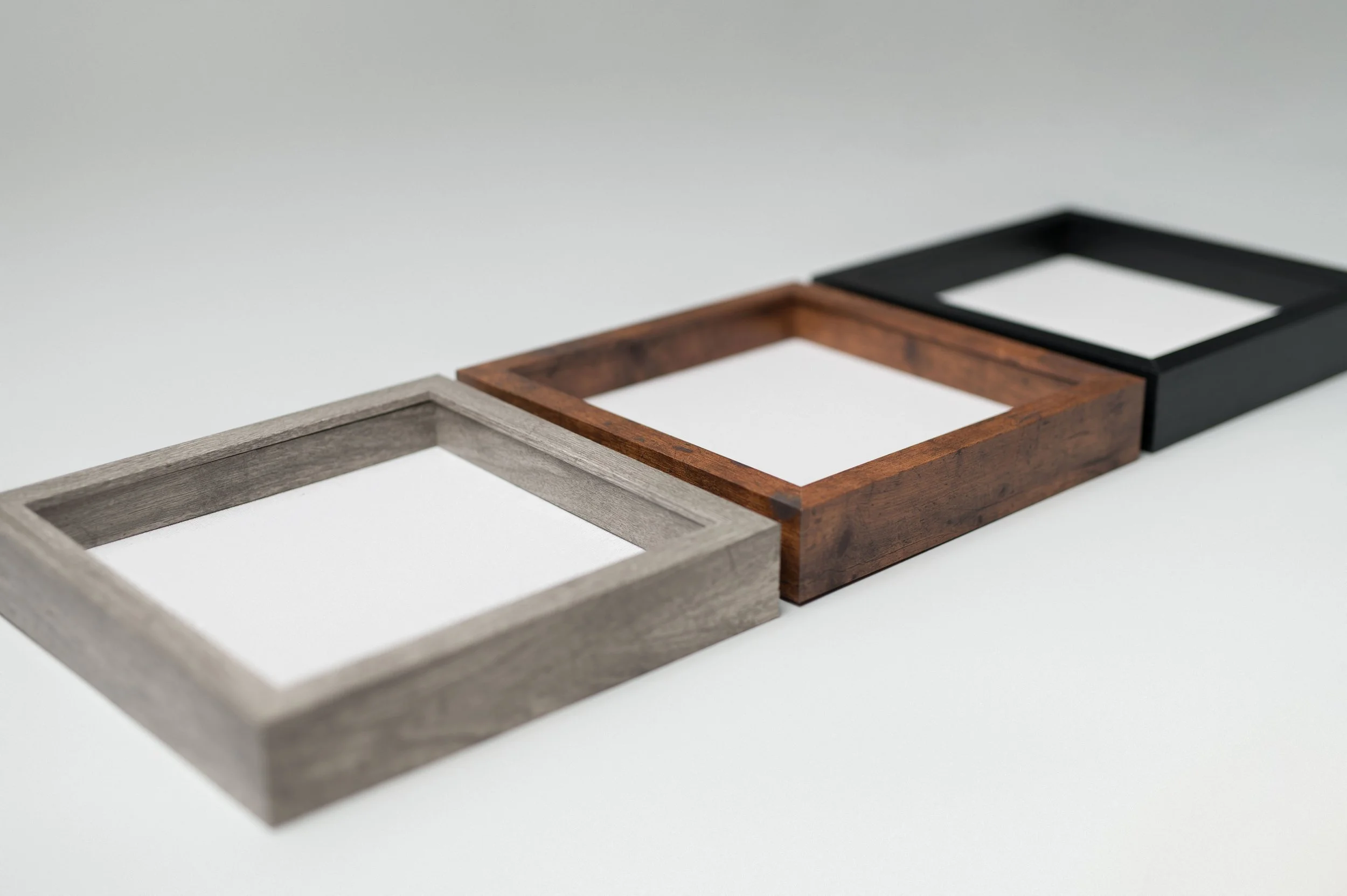 Four empty rectangular shadow box frames made of different types of wood, arranged in a diagonal line on a plain white background.