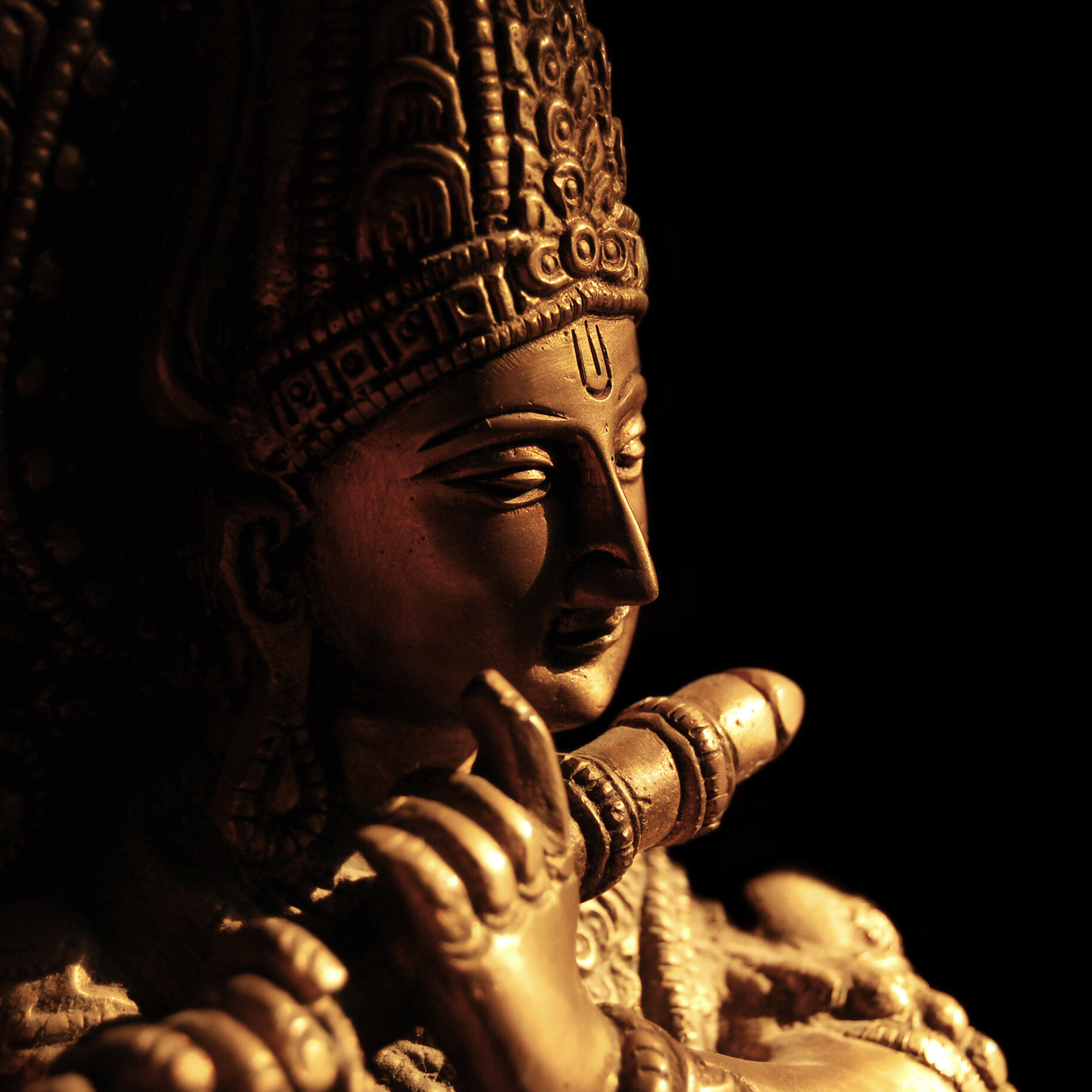 Close-up of a golden Hindu deity or goddess statue, with detailed headgear and a hand near the face, against a dark background.