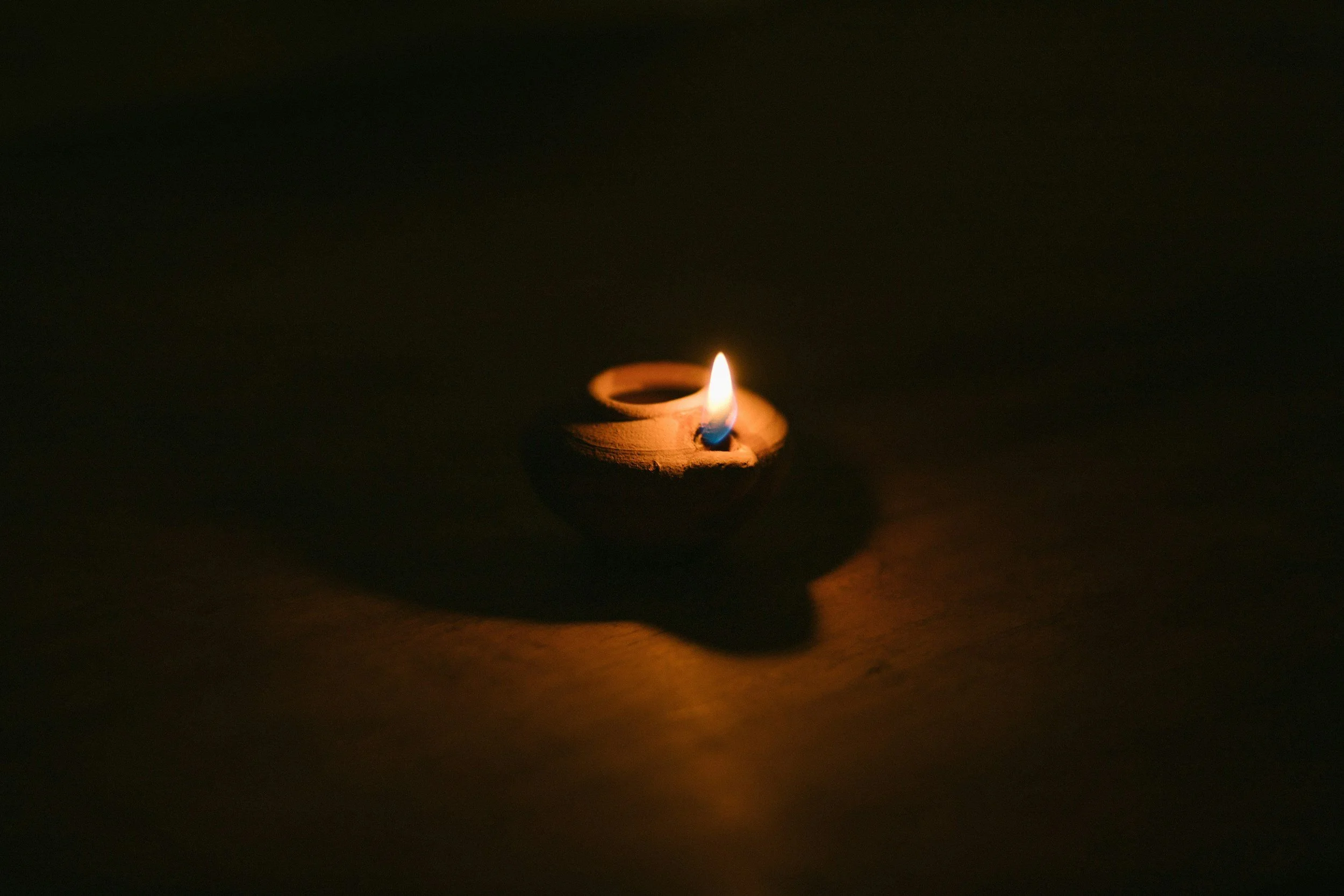 A lit clay diya oil lamp casting a glow in darkness.