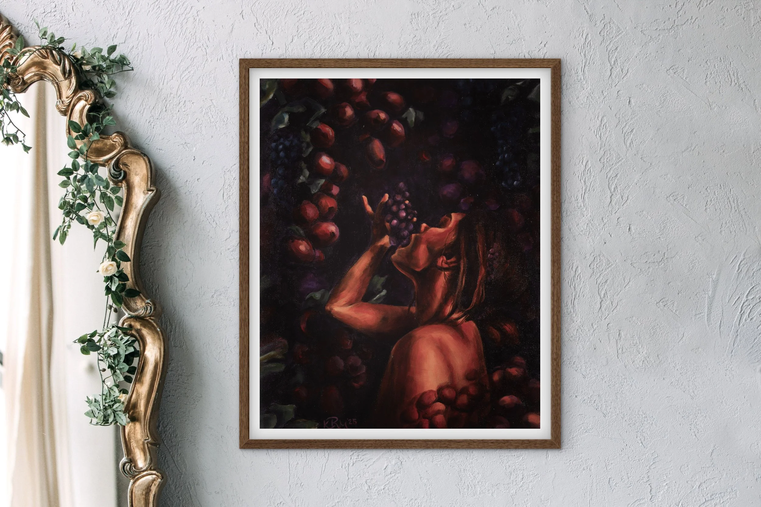 A framed painting of a woman with long hair surrounded by dark grapes, holding a bunch of grapes close to her lips, on a textured white wall, with an ornate mirror with greenery on the left side.