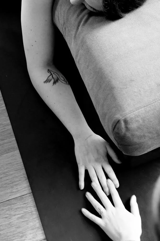 A person with a tattoo on their left forearm is reaching out and touching another person's hand, which is resting on a yoga mat.