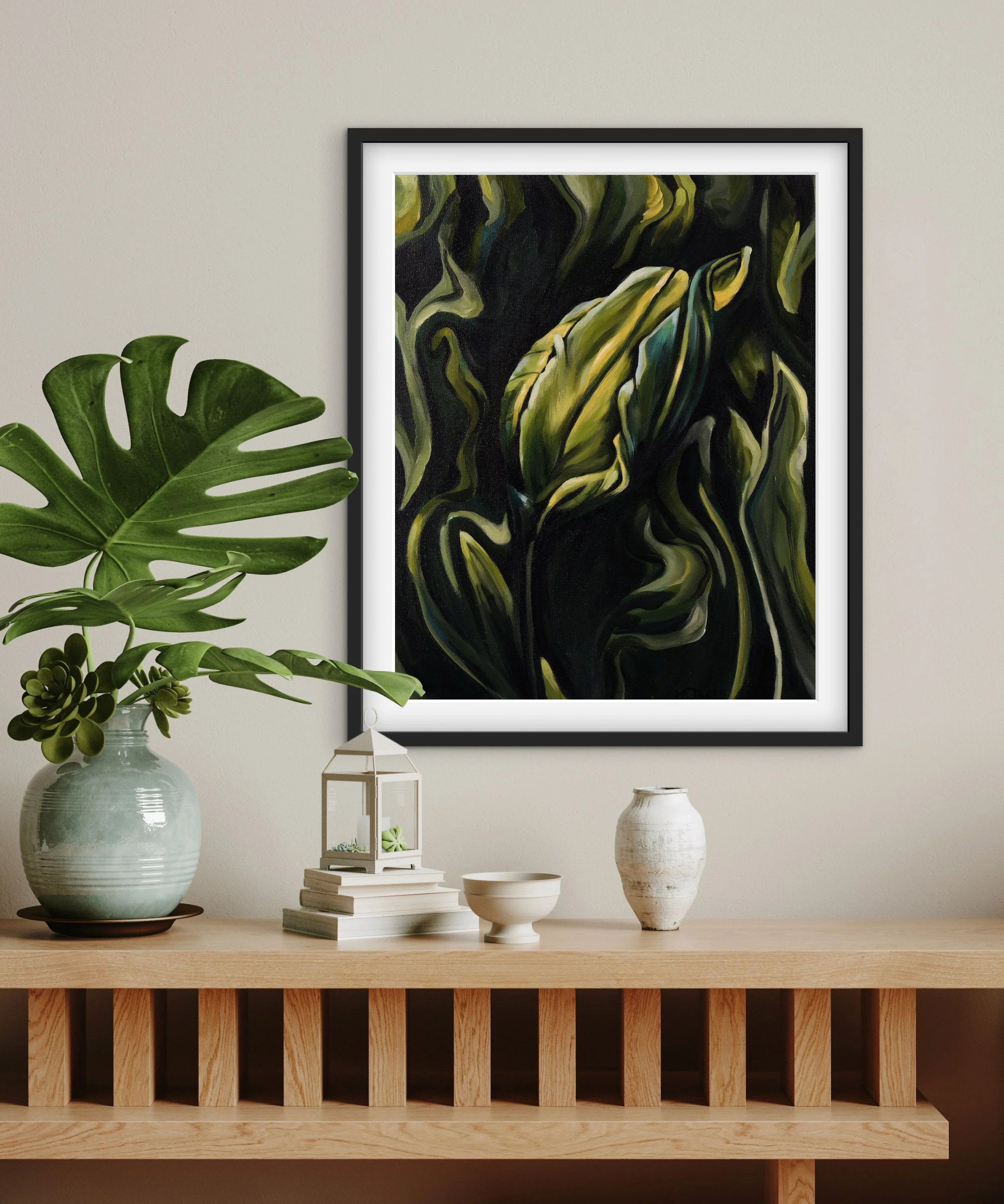 Decorative wall with framed abstract botanical artwork, large monstera plant, and smaller succulents on wooden console table.