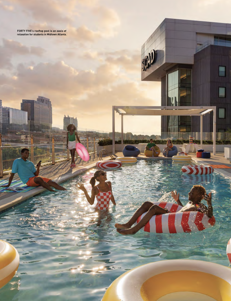 People enjoying a rooftop pool at sunset with city skyline in the background, with inflatable floaties and lounge chairs.